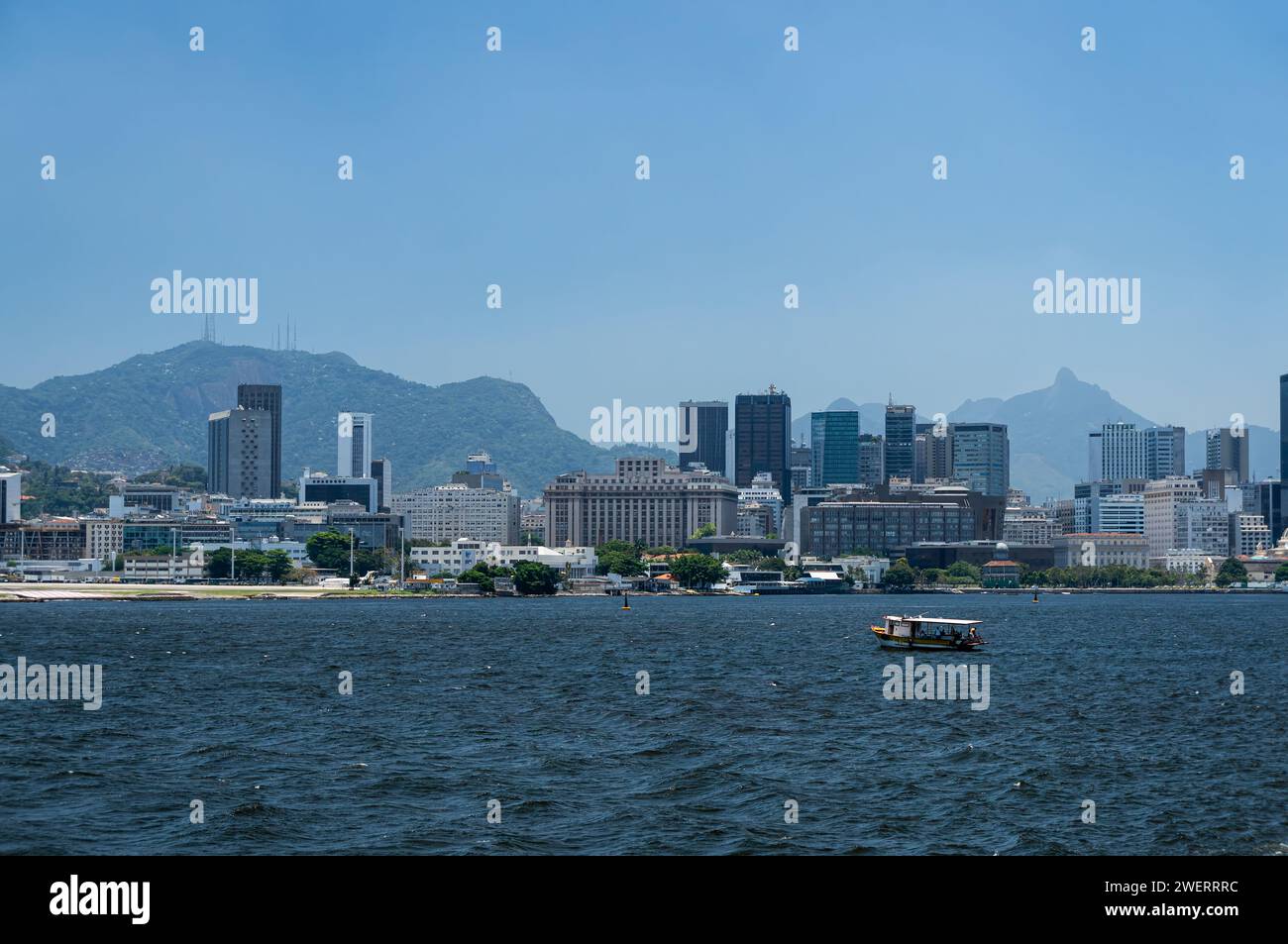 Gli edifici del quartiere Centro sul lungomare sono visti dalla costa della baia di Guanabara e dalle acque blu vicino all'aeroporto Santos Dumont sotto il cielo blu del pomeriggio estivo. Foto Stock