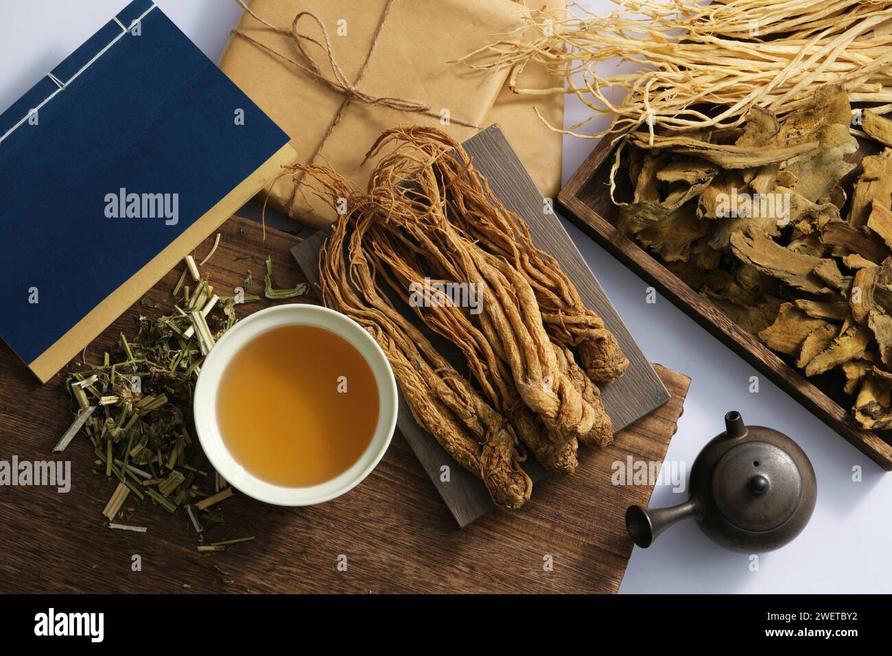 Radici di Angelica sinensis su un vassoio rettangolare, coppa di medicina, libro blu, pacchetto di medicine e alcune erbe essiccate su sfondo chiaro. Scena per la pubblicità Foto Stock