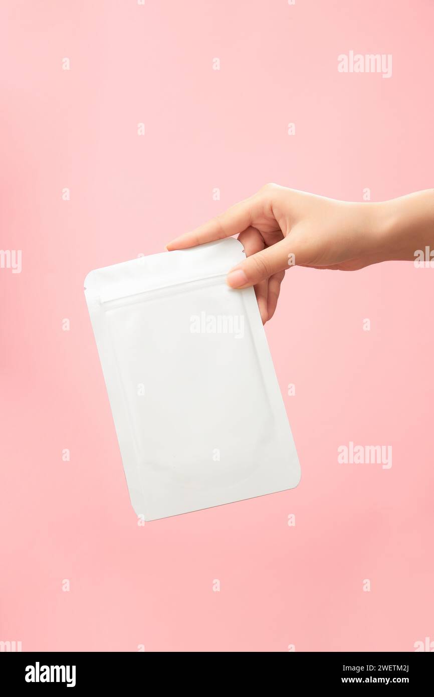 Vista frontale della mano femminile che regge un modellino di mascherina facciale su sfondo rosa. Scene pubblicità prodotti di bellezza, maschere idratanti, whi Foto Stock