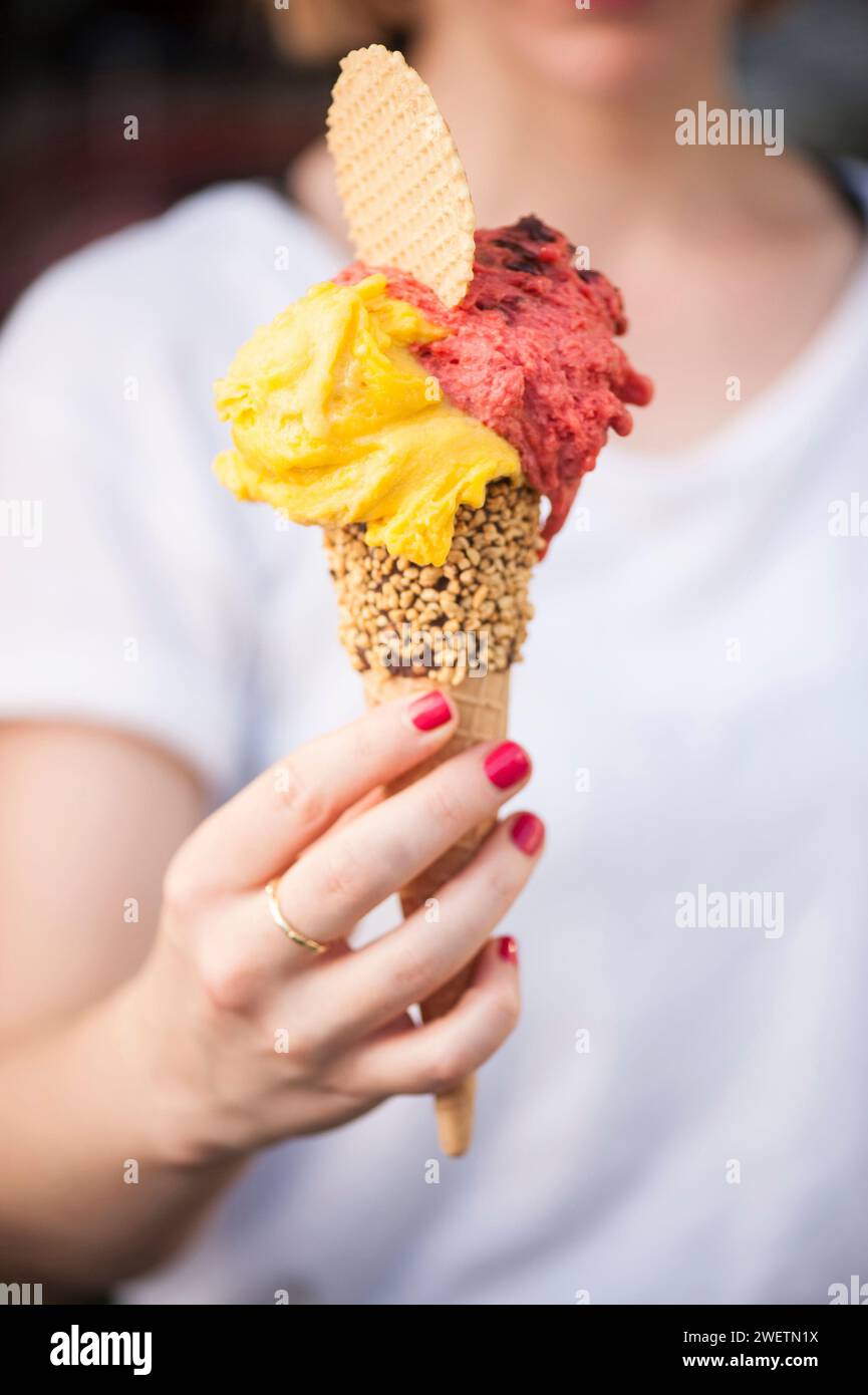 Ragazza che tiene un gelato giallo e color pesca a cono, Italia Foto Stock