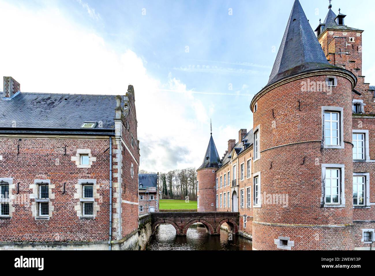 Fossato che circonda il castello di Alden Biesen del XVI secolo, ponte tra due edifici e alberi nudi sullo sfondo, torri circolari, mura in mattoni e spioventi Foto Stock