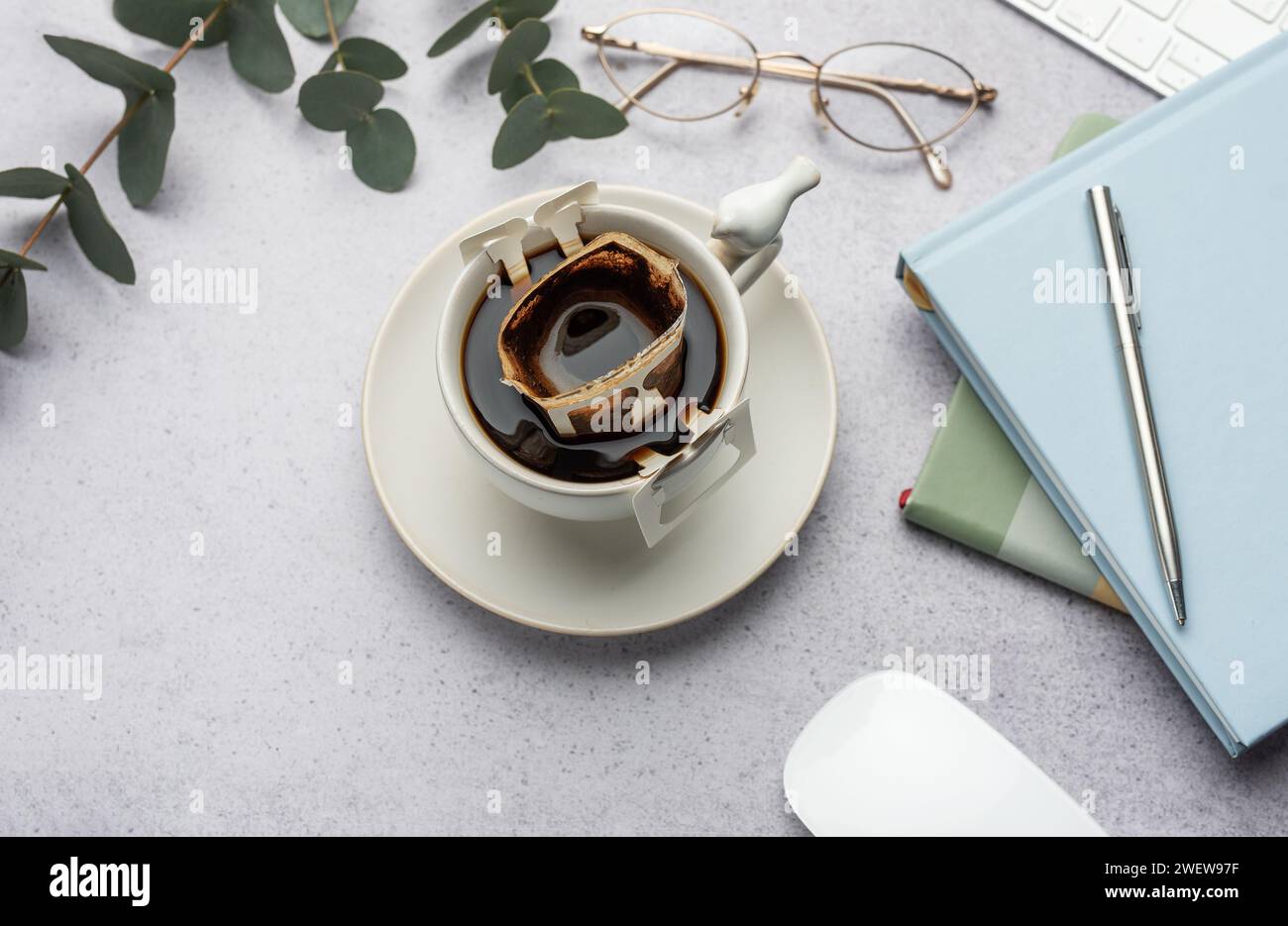 Una tazza di caffè appena fatto con un pratico filtro antigoccia sul tavolo da ufficio. Pausa caffè, un modo veloce per preparare una bevanda calda Foto Stock