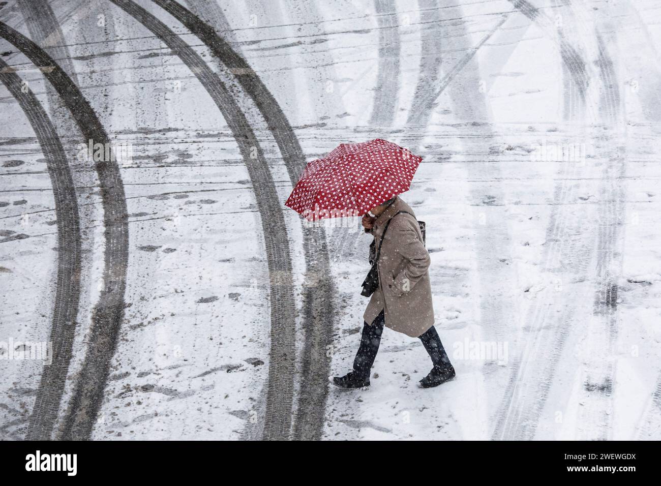 Donna con un ombrello punteggiato rosso e bianco attraversa una strada coperta di neve nel centro della città, neve, inverno, Colonia, Germania. 17 gennaio. 2024 Frau mit Foto Stock