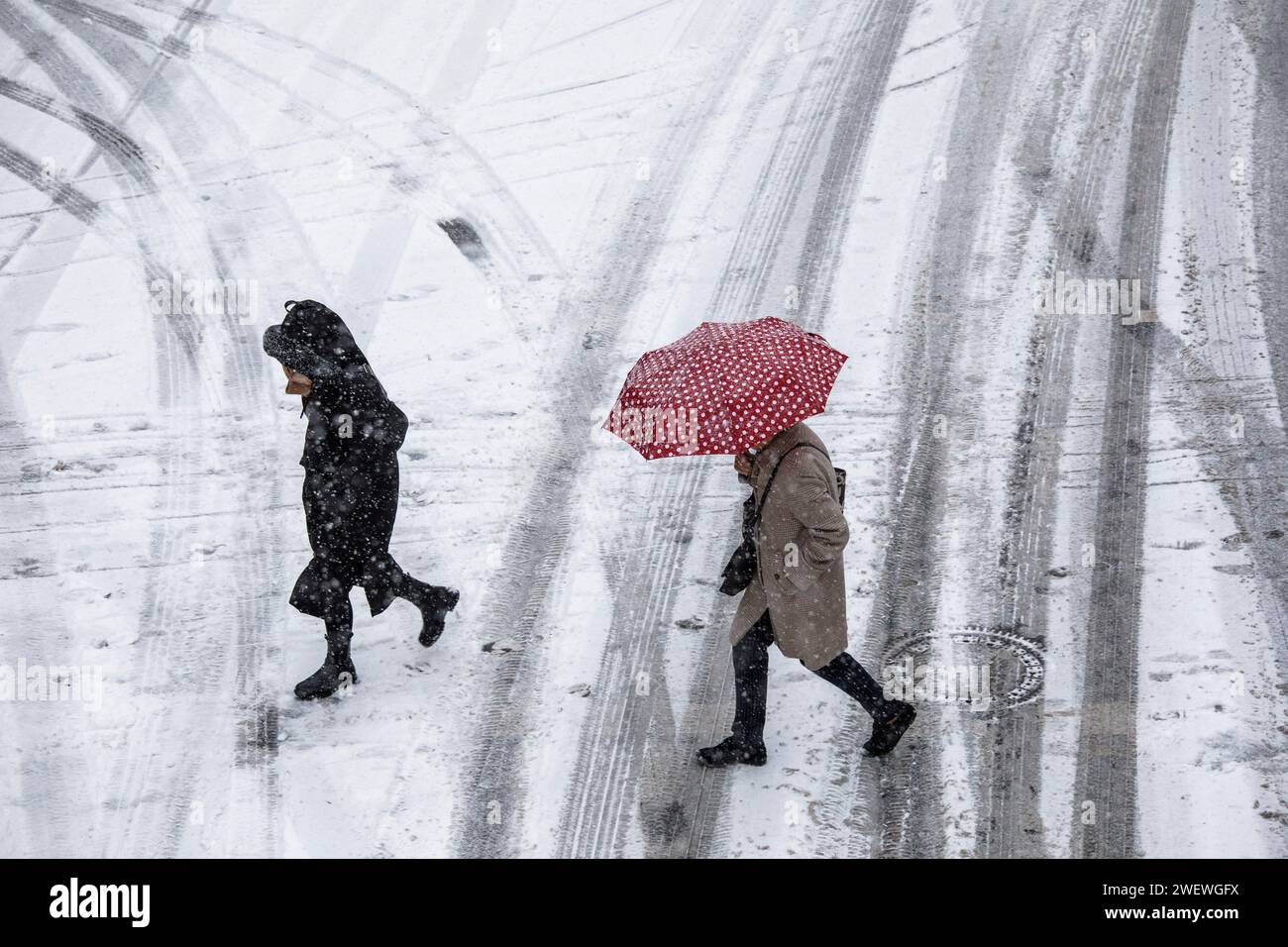 Donna con un ombrello punteggiato rosso e bianco attraversa una strada coperta di neve nel centro della città, neve, inverno, Colonia, Germania. 17 gennaio. 2024 Frau mit Foto Stock