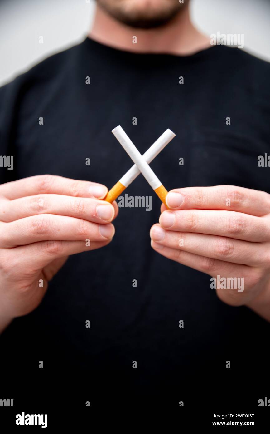 un uomo che tiene due sigarette che ne crea una croce Foto Stock