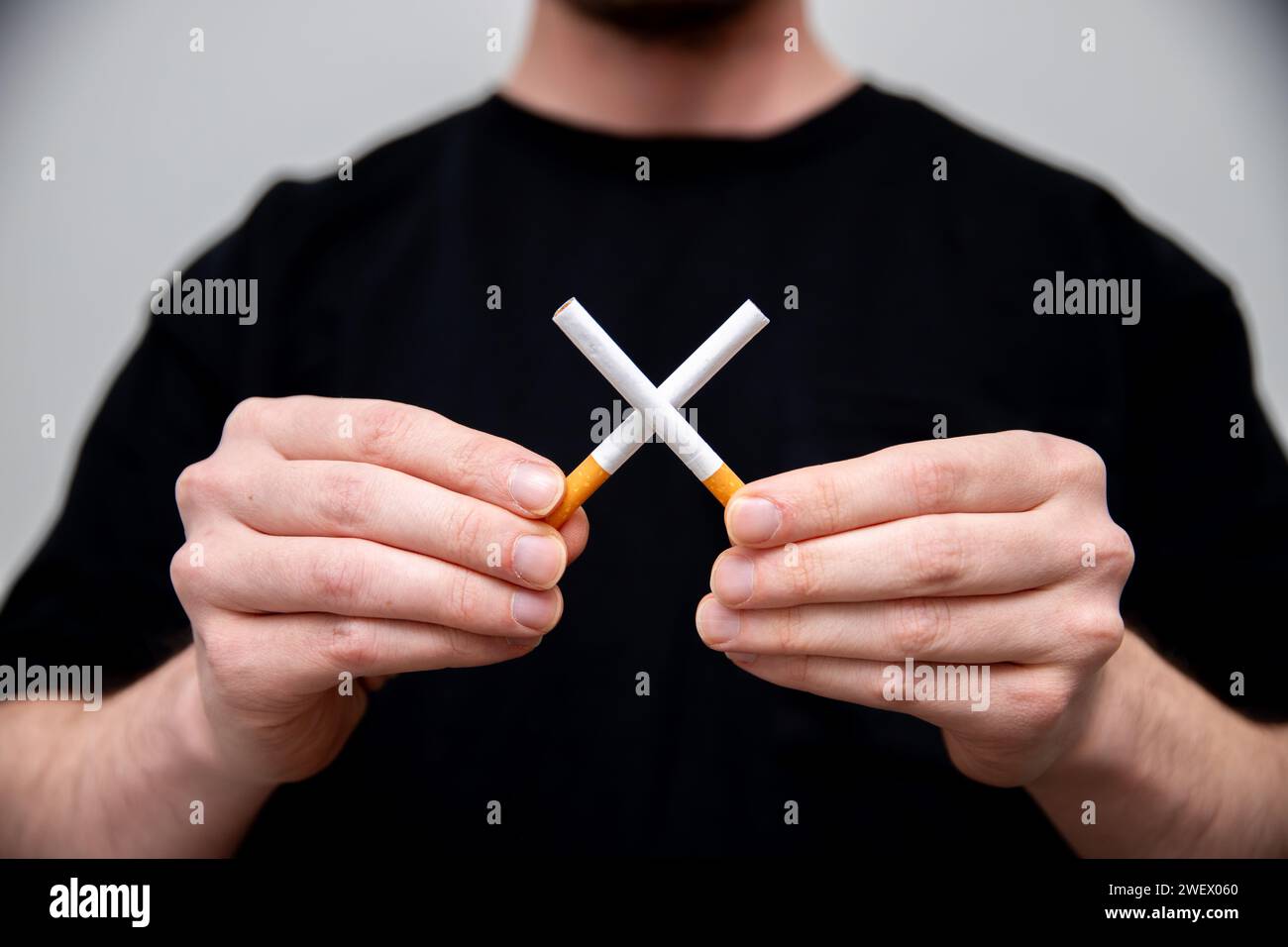 un uomo che tiene due sigarette che ne crea una croce Foto Stock