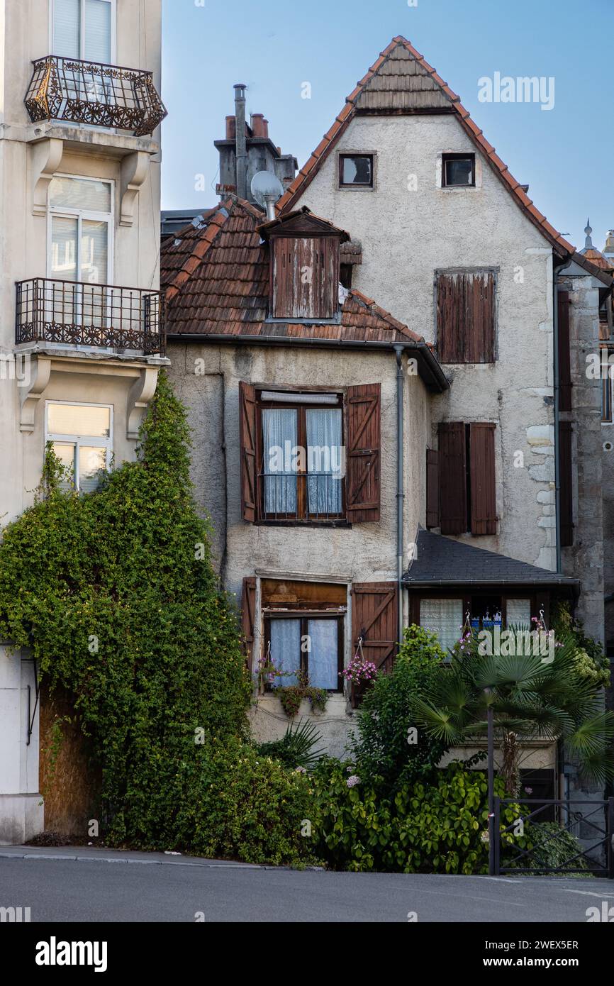 Una tradizionale casa marrone-grigia con tetto in piastrelle rosse e persiane, intrecciata con edera e palme. Pau, Pyrénées-Atlantiques, Francia. Foto Stock