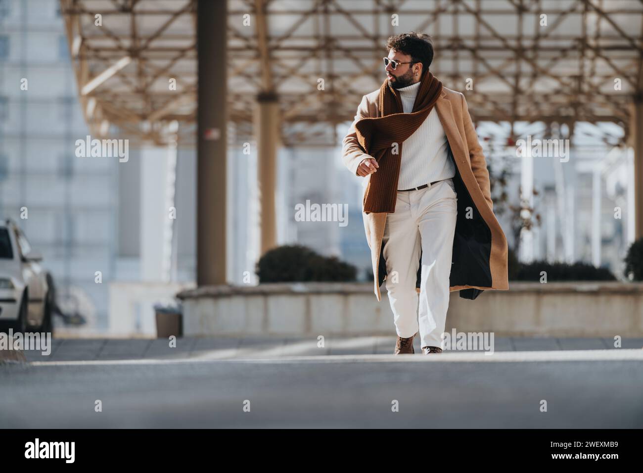 Uomo elegante con soprabito che cammina con sicurezza in un ambiente urbano. Foto Stock