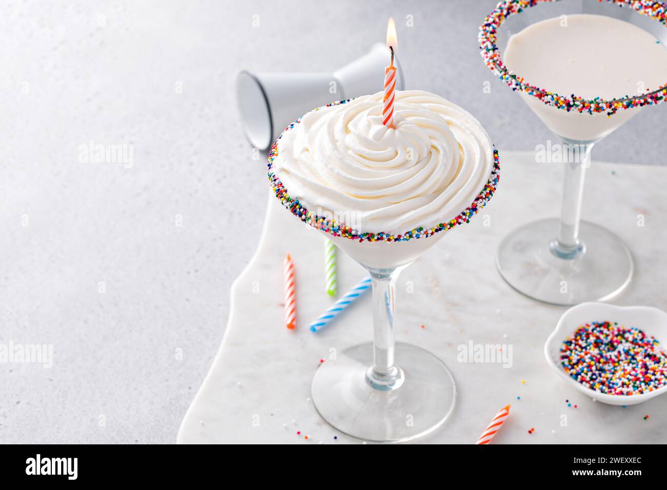 Cocktail martini con torta di compleanno condito con panna montata e una candela di compleanno e spolverini Foto Stock