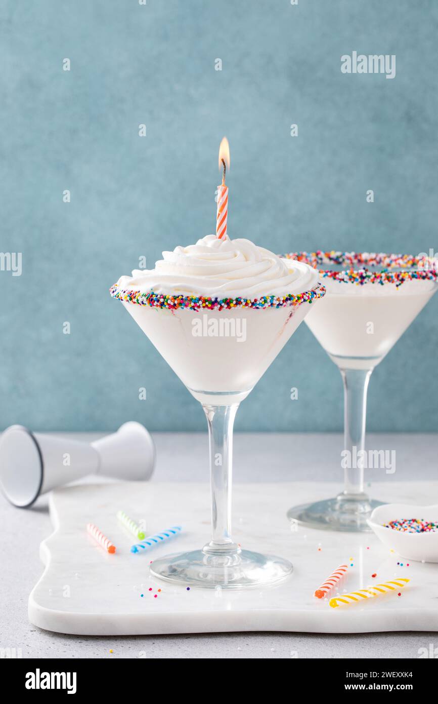 Cocktail martini con torta di compleanno condito con panna montata e una candela di compleanno e spolverini Foto Stock