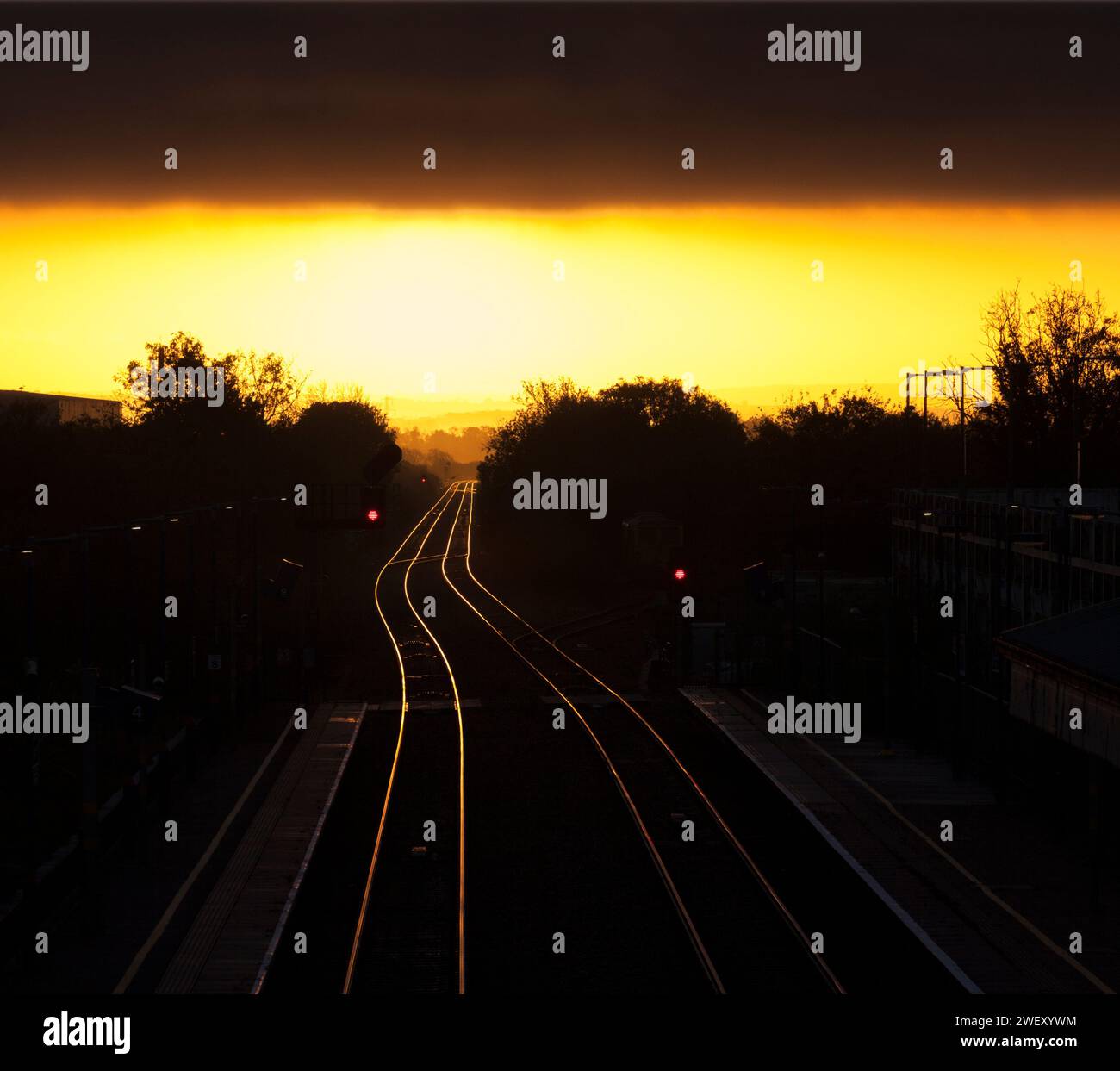 Alba alla stazione ferroviaria di Bicester North sulla linea principale di Chiltern con il sole dorato che splende fuori dalla linea ferroviaria con segnali luminosi colorati. Foto Stock