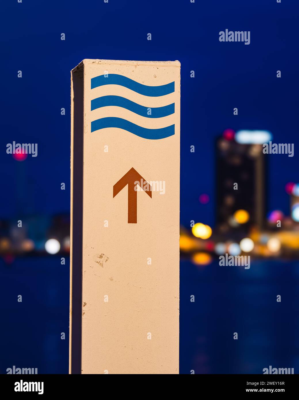 Un cartello con i simboli delle onde blu e una freccia rivolta verso l'alto è ben messo a fuoco su uno sfondo sfocato di vivaci luci notturne della città. Foto Stock