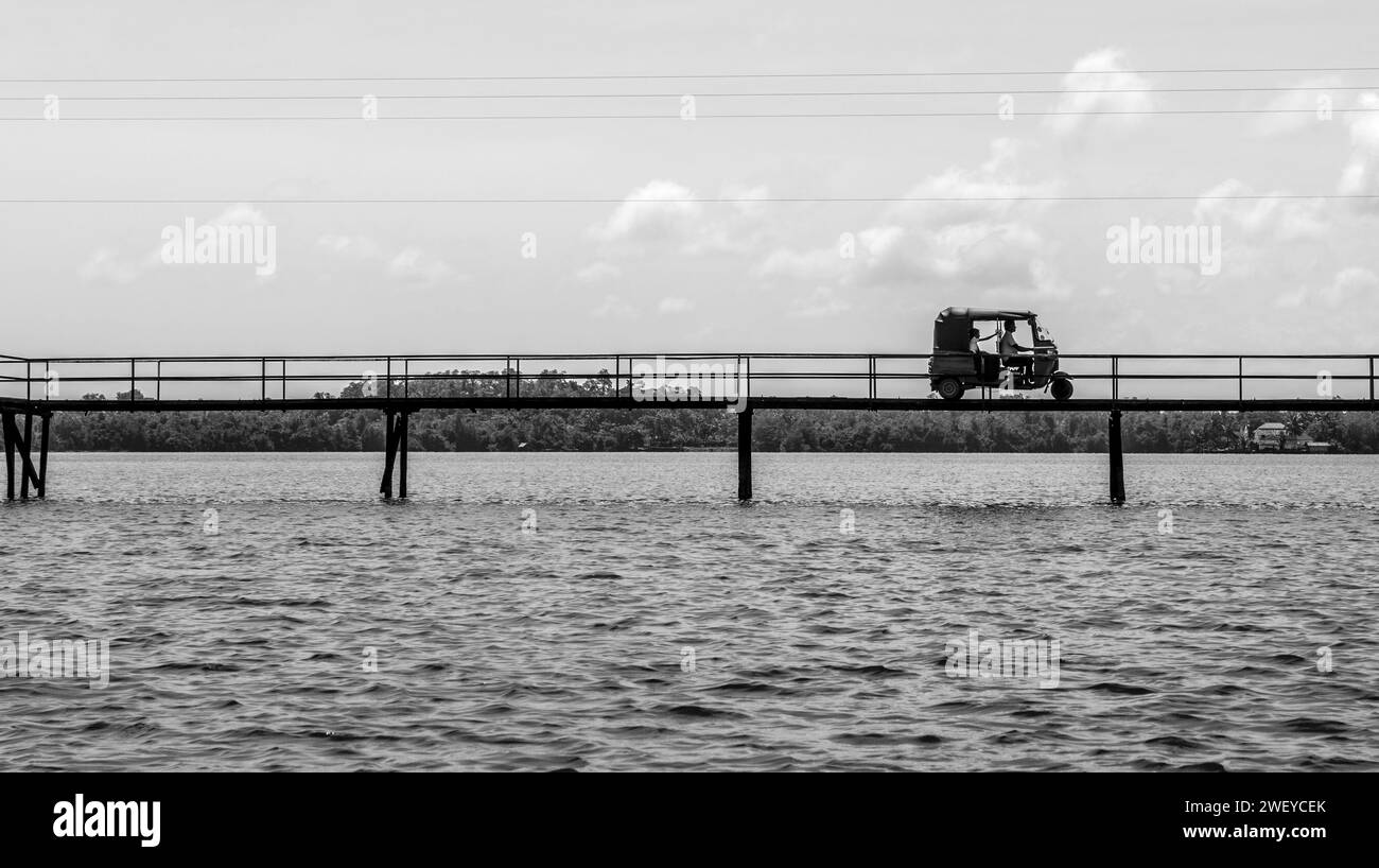 Un'auto tuk tuk viaggia su un ponte sull'acqua nello Sri Lanka Foto Stock