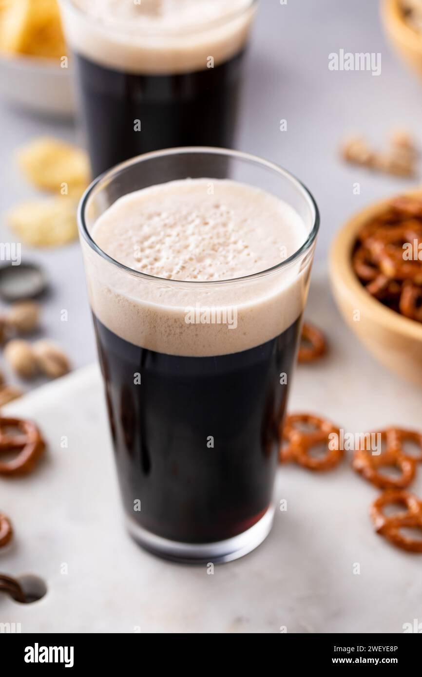 Birra scura in bicchieri alti con noci, pretzel e patatine fritte Foto Stock