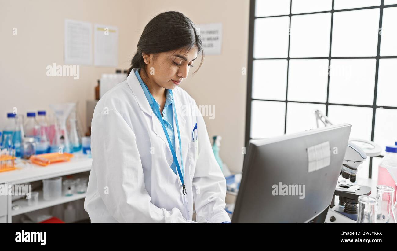 Una scienziata indiana concentrata analizza i dati su un computer in un ambiente di laboratorio, mostrando la sua professionalità. Foto Stock