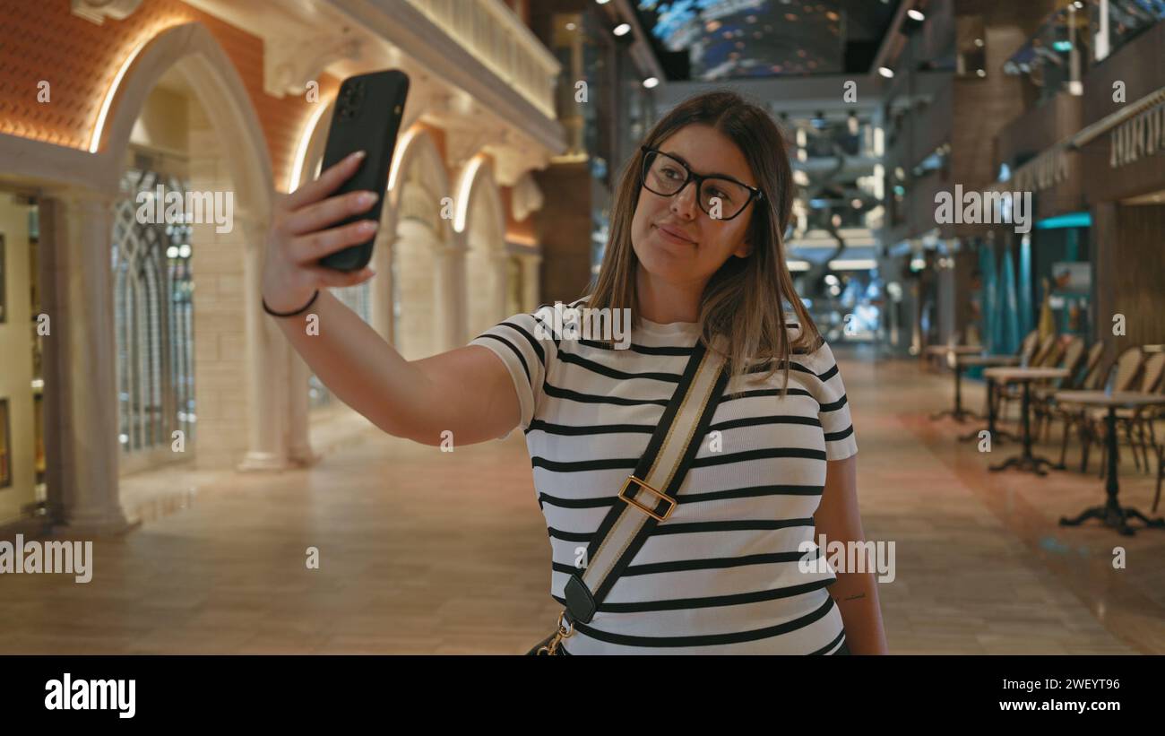 Una giovane donna scatta un selfie all'interno di una moderna e lussuosa nave da crociera con un sofisticato design degli interni. Foto Stock