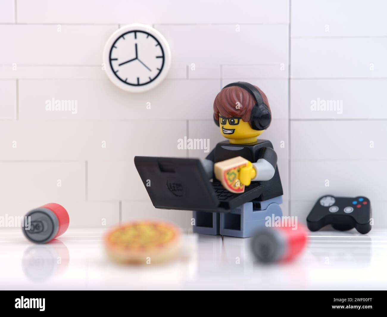 Tambov, Federazione Russa - 27 gennaio 2024 Un personaggio di un videogioco Lego seduto sul pavimento, che gioca ai videogiochi su un computer portatile e mangia una pizza Foto Stock