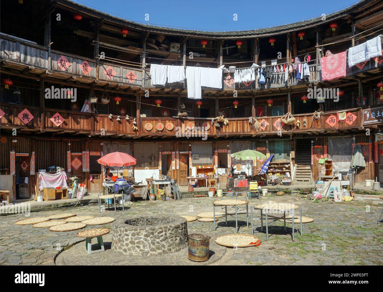 Essiccazione del raccolto e del grano nel cortile di un Hakka Tulou (edificio fatto di terra e legno speronato) nella contea di Nanjing, Fujian, Cina Foto Stock