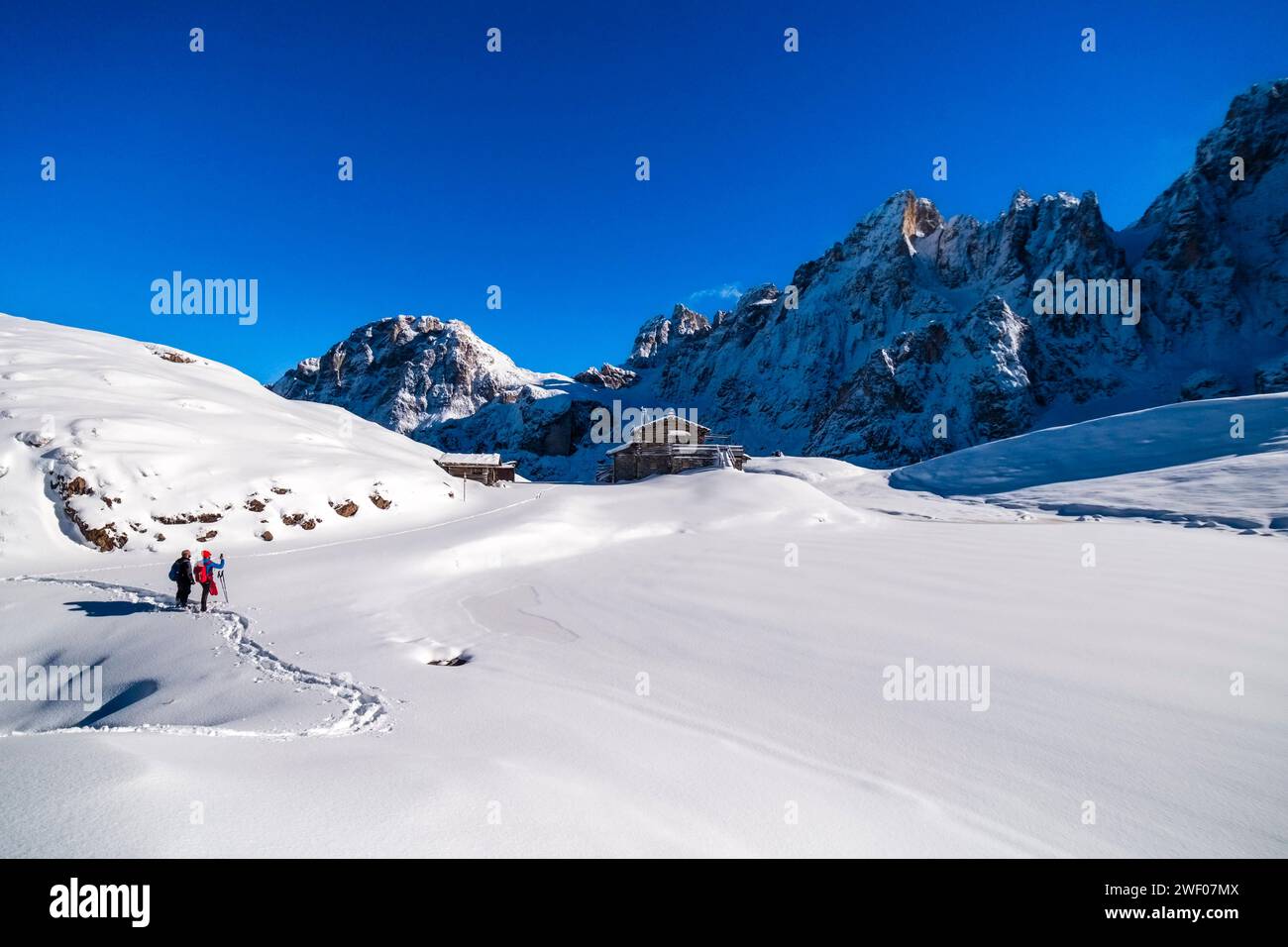 Due escursionisti con le ciaspole che camminano fino al rifugio Baita Segantini, le cime del gruppo pale in lontananza, in inverno. San Martino di Castrozza TR Foto Stock