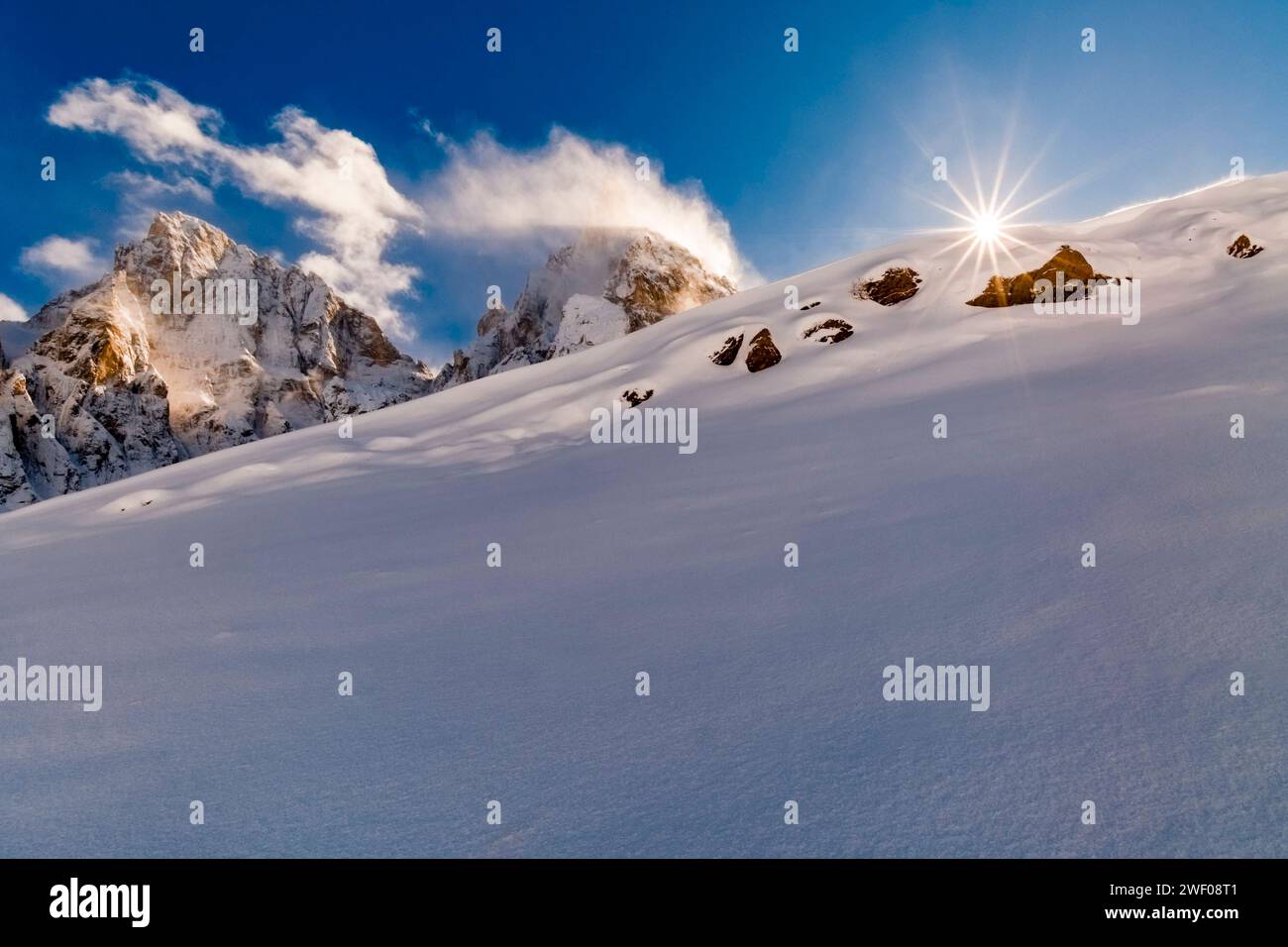 Il sole splende su strutture di neve alla deriva su una collina in Val Venegia sopra il passo Rolle, le cime di cima della Vezzana a sinistra e Cimon della Pal Foto Stock
