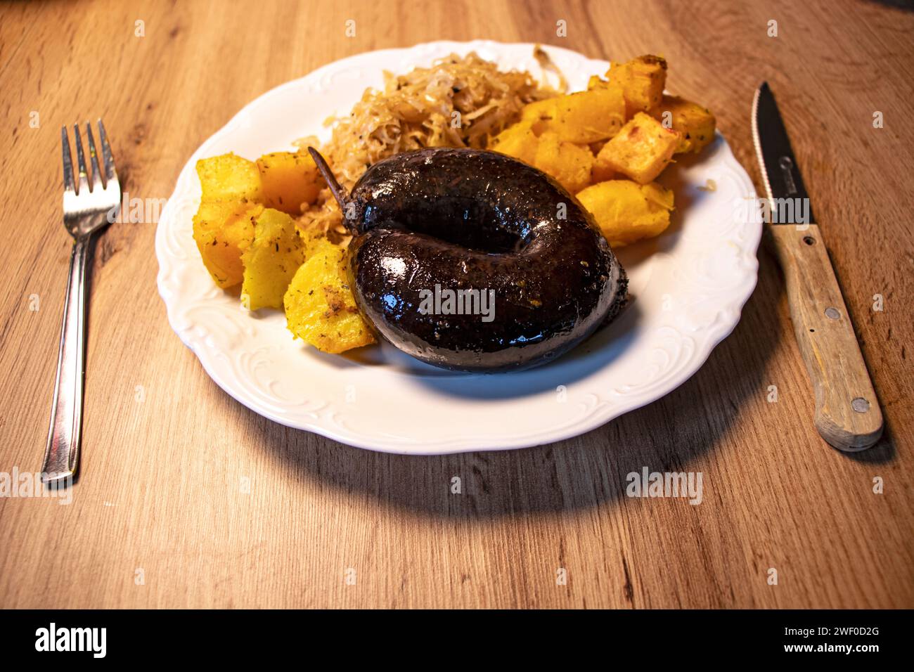 Salsiccia arrosto con patate e cavolo su piatto bianco su tavola di legno Foto Stock