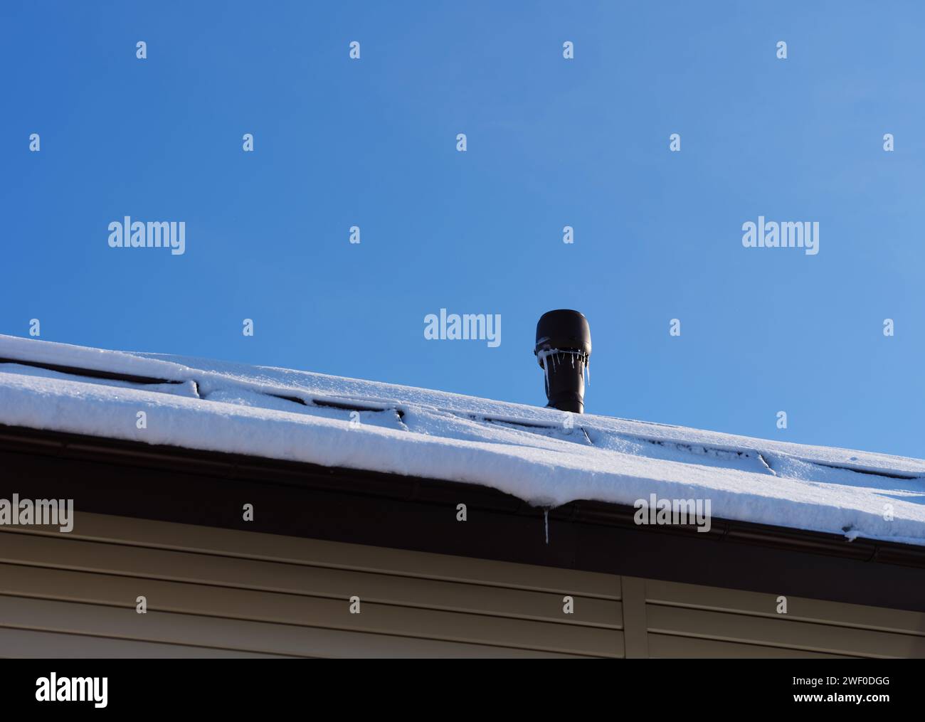 Una pila di bocchette con ghiaccio su un tetto innevato su sfondo blu. Foto Stock