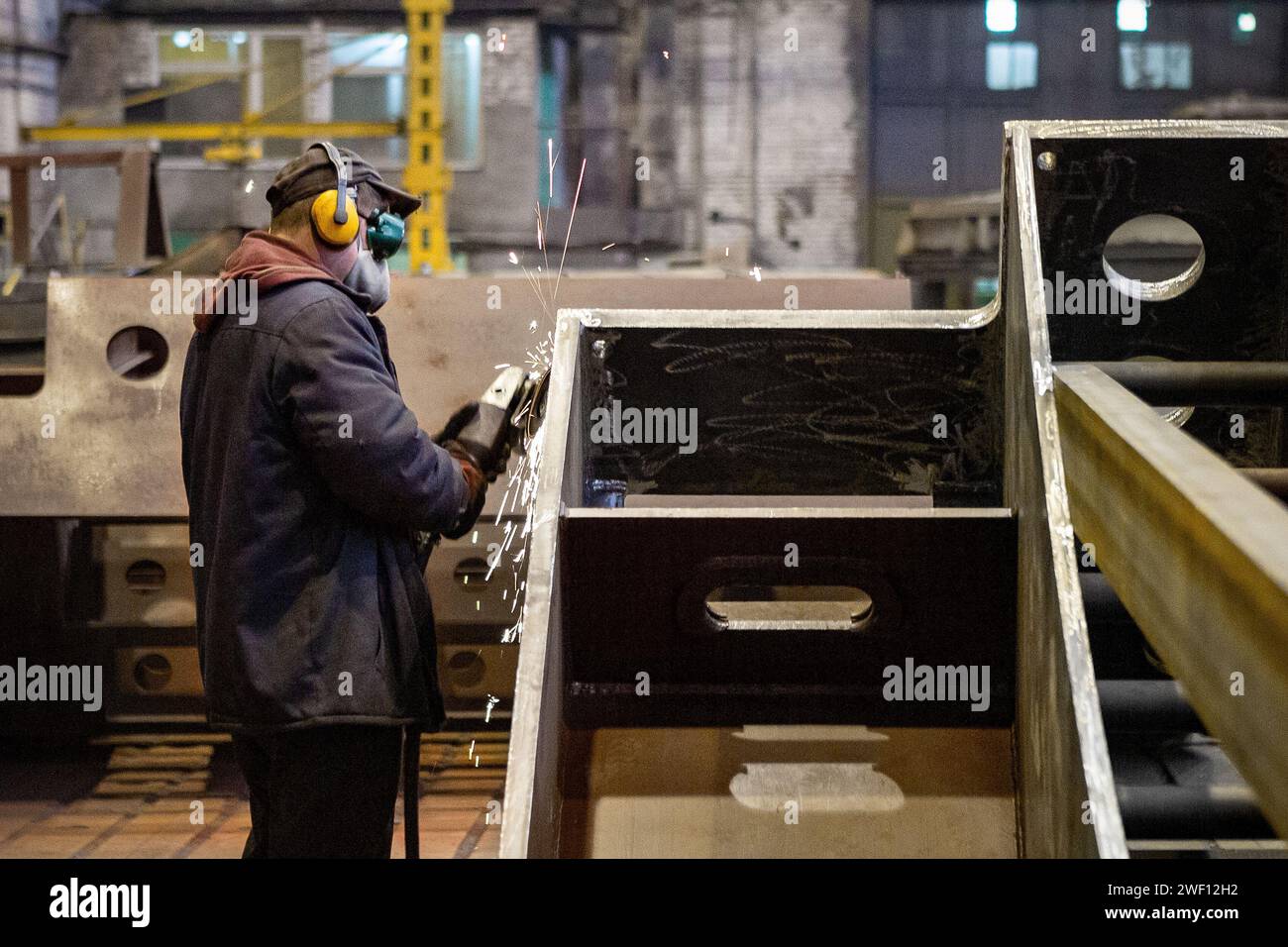 Lavoratore in maschera smeriglia una parte metallica in fabbrica o la taglia con una sega circolare elettrica. Foto Stock