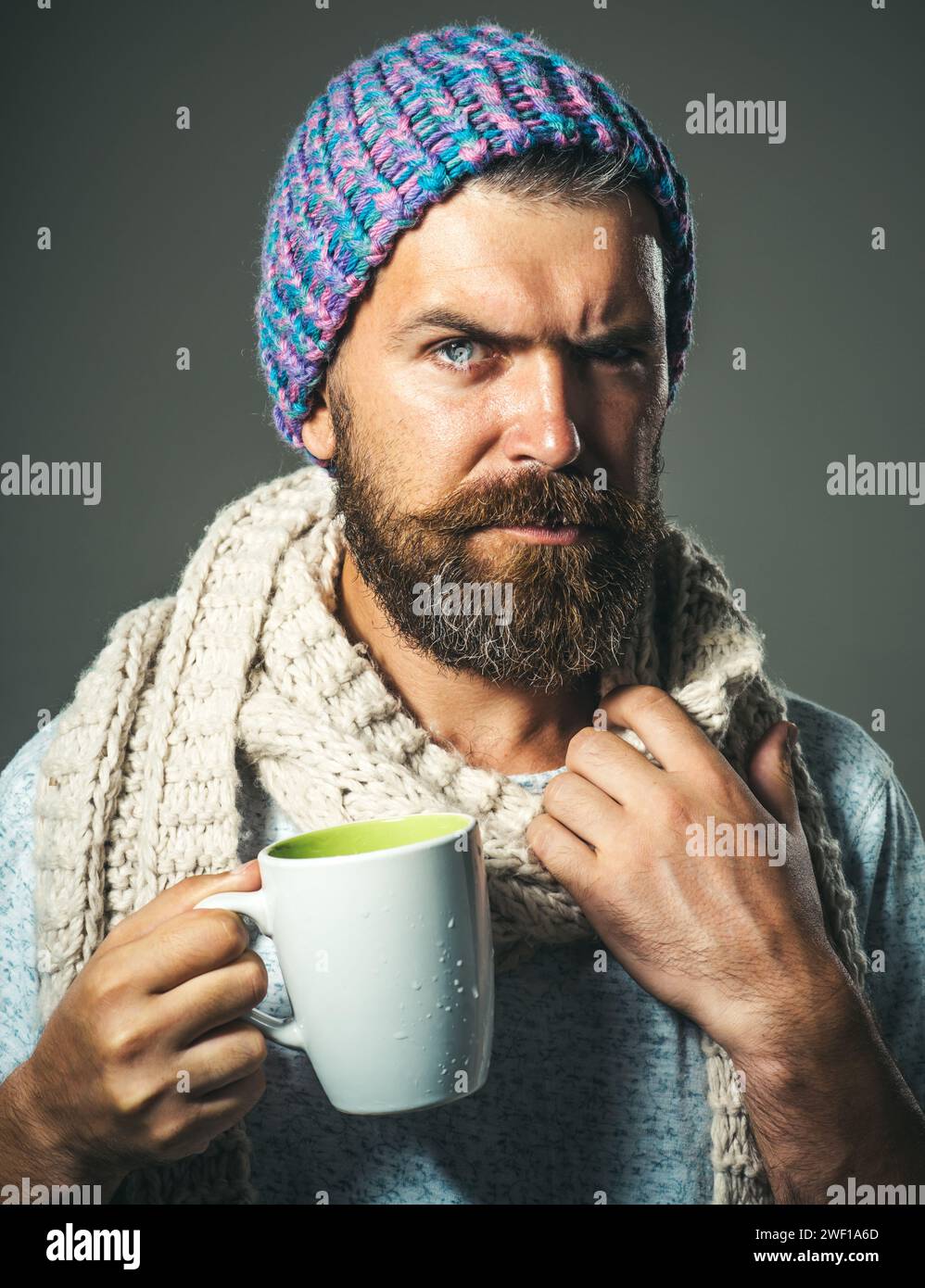 Bell'uomo elegante con abiti alla moda che beve bevande dalla tazza. Maschio barba serio in maglione avvolto in sciarpa bianca con tazza di caffè caldo Foto Stock