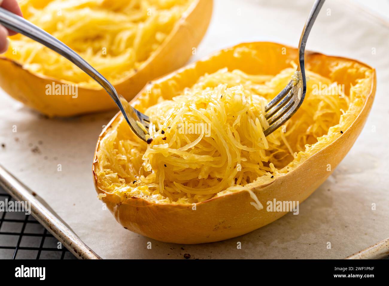 Spaghetti di zucca cotti al forno e tagliati a pezzi con due forchette, pronti da mangiare su una teglia da forno Foto Stock