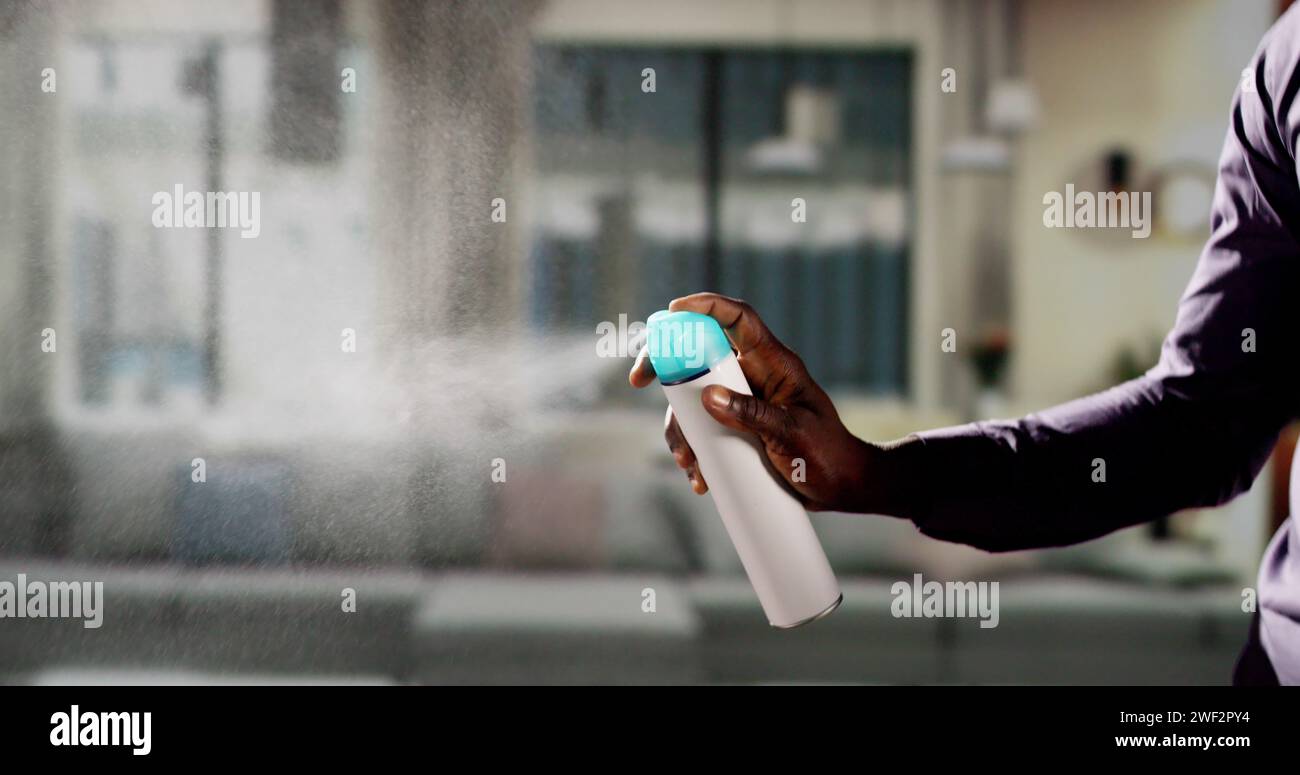 Uomo africano che usa l'aria spray nel soggiorno Foto Stock