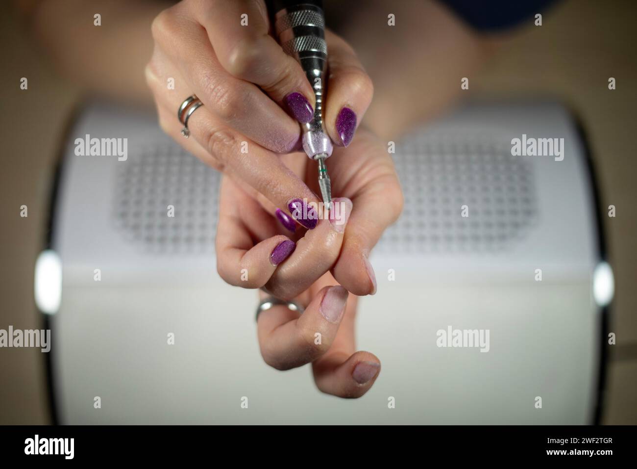 Primo piano dettagliato di cuticola caucasica irriconoscibile con lima per unghie elettrica sopra un collettore di polvere, manicure fai da te Foto Stock