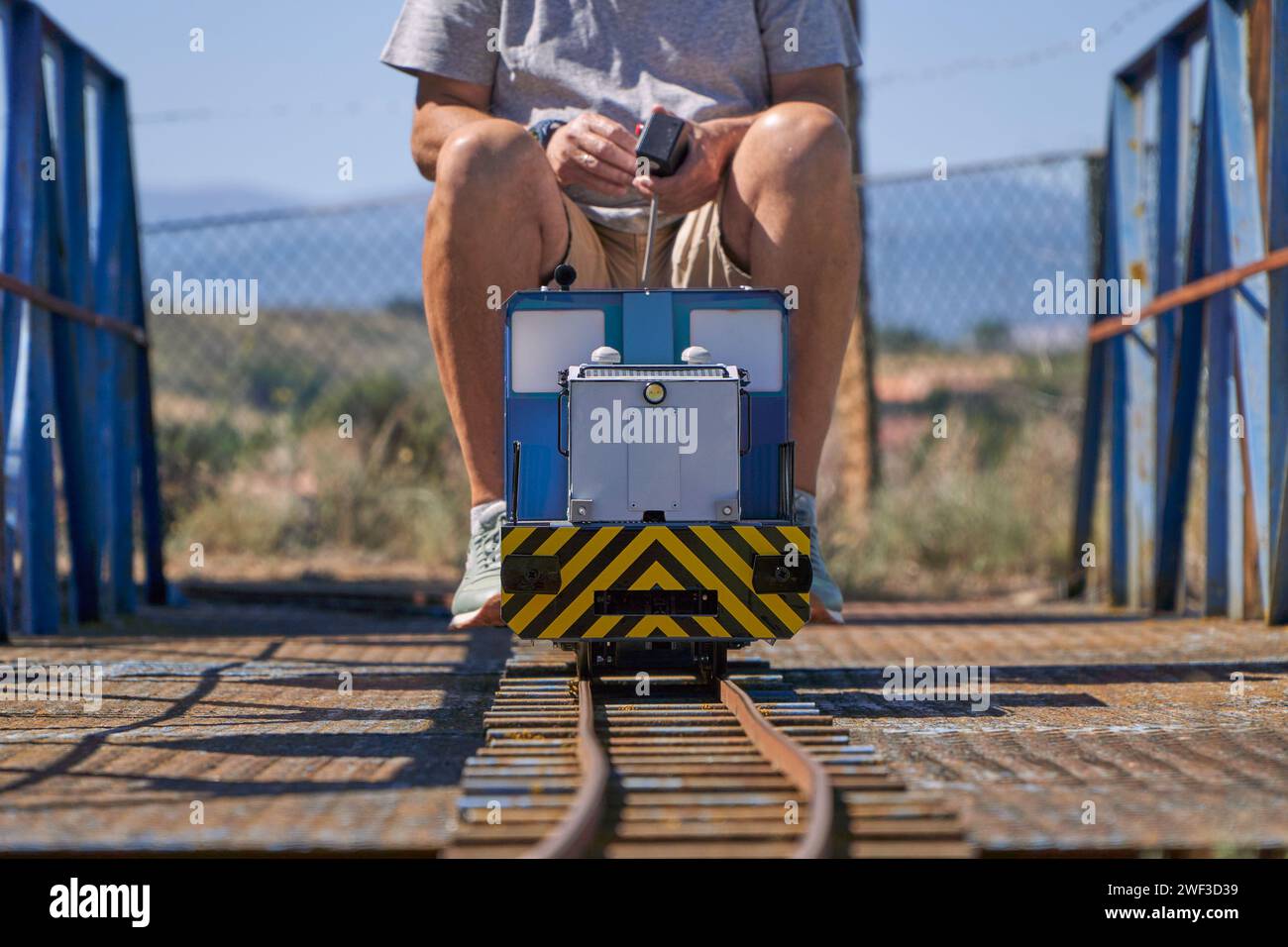 Uomo maturo che gioca con un treno elettrico a scartamento di 5 cm su una vecchia e arrugginita ferrovia all'aperto Foto Stock