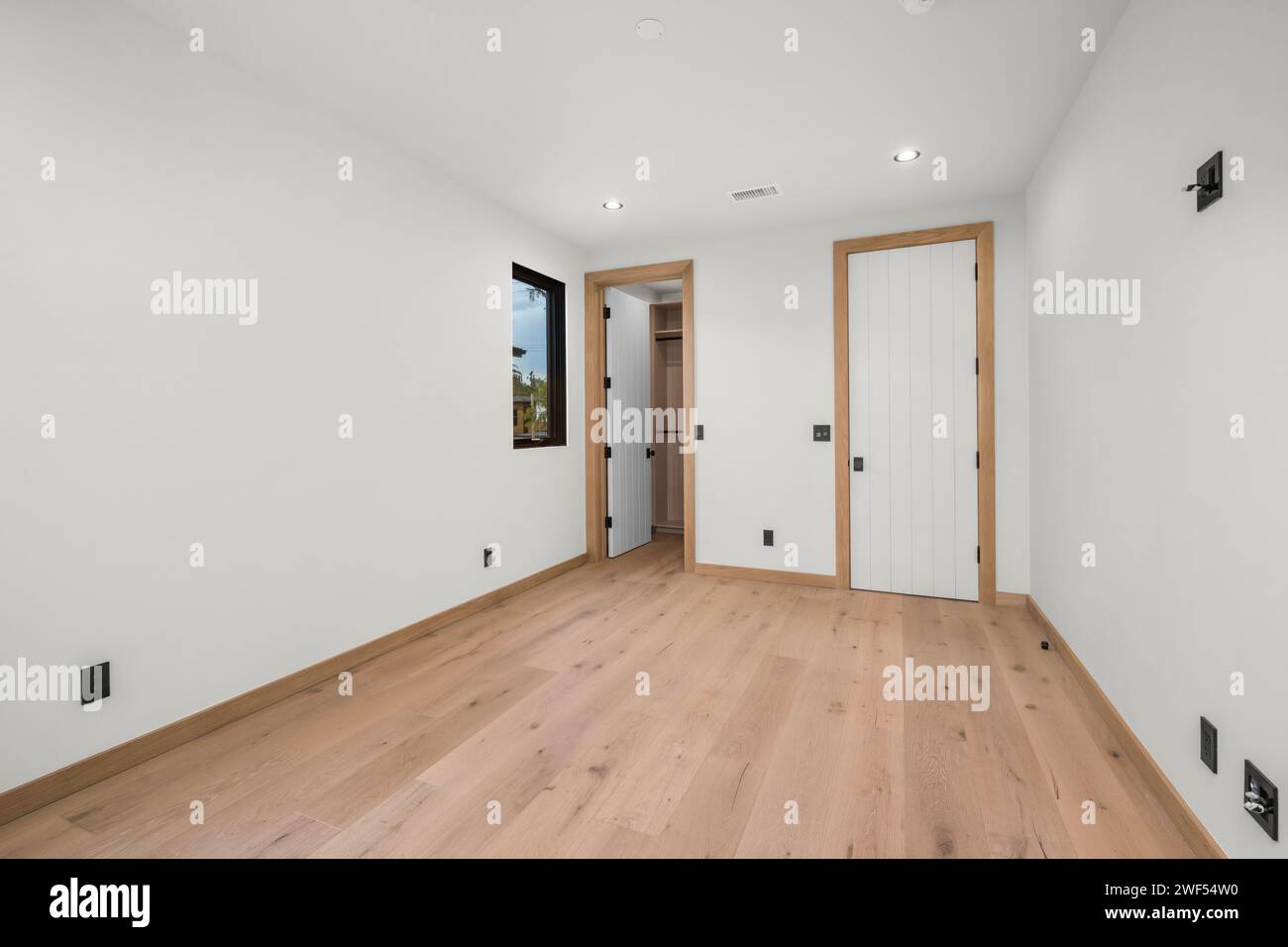 Una stanza vuota con pavimenti in legno, una porta, una finestra e persiane parzialmente chiuse Foto Stock