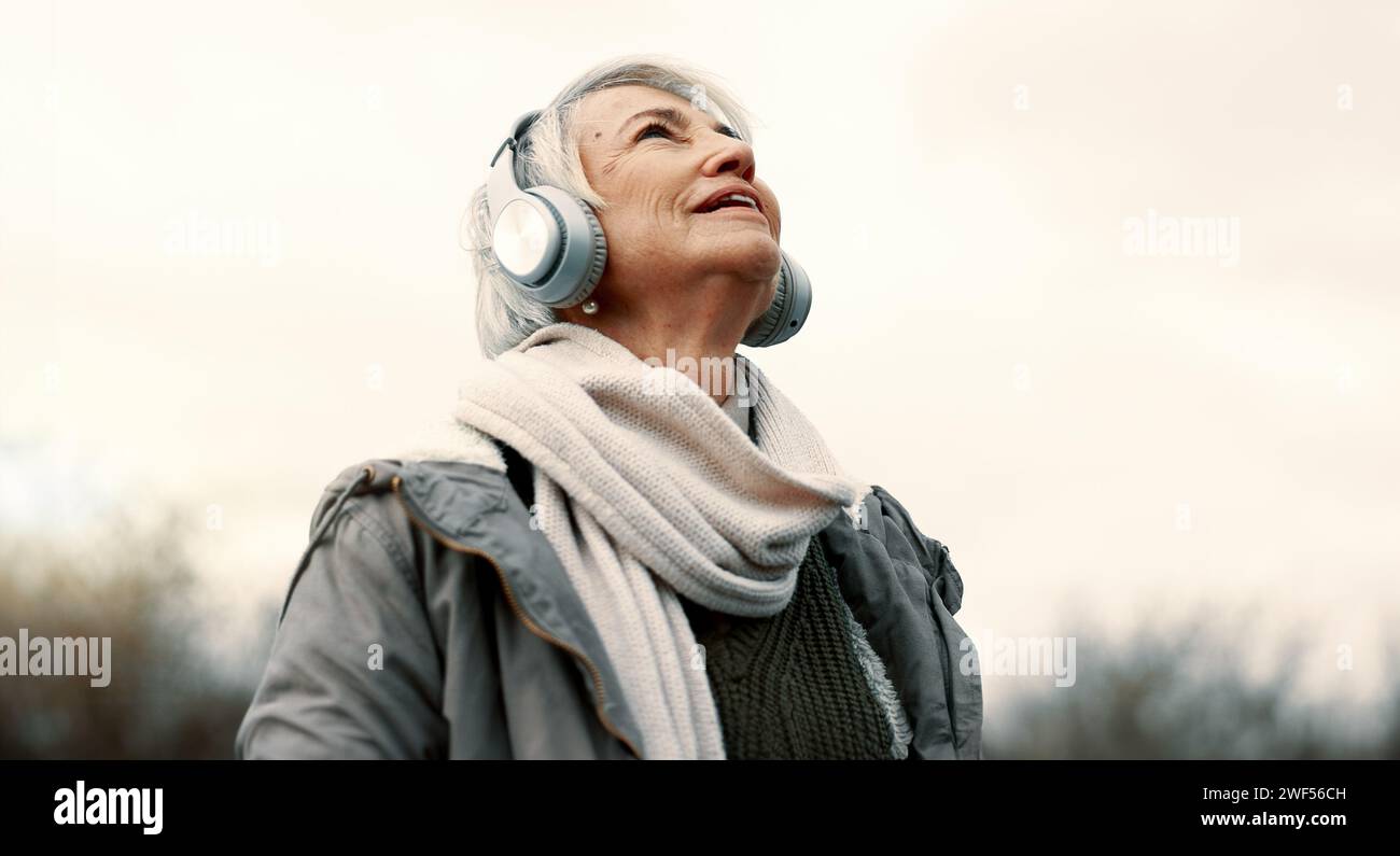 Cuffie, musica e donna anziana in natura per il benessere, la salute mentale e felice esperienza all'aperto. Servizi di viaggio, ascolto e streaming o. Foto Stock