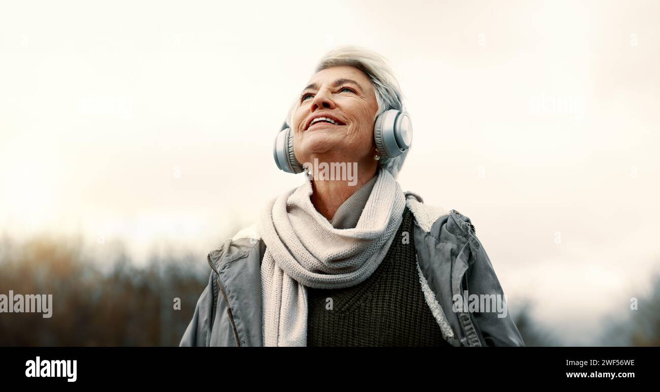 Cuffie, musica e donna anziana in natura per il benessere, la salute mentale e felice esperienza all'aperto. Servizi di viaggio, ascolto e streaming o. Foto Stock