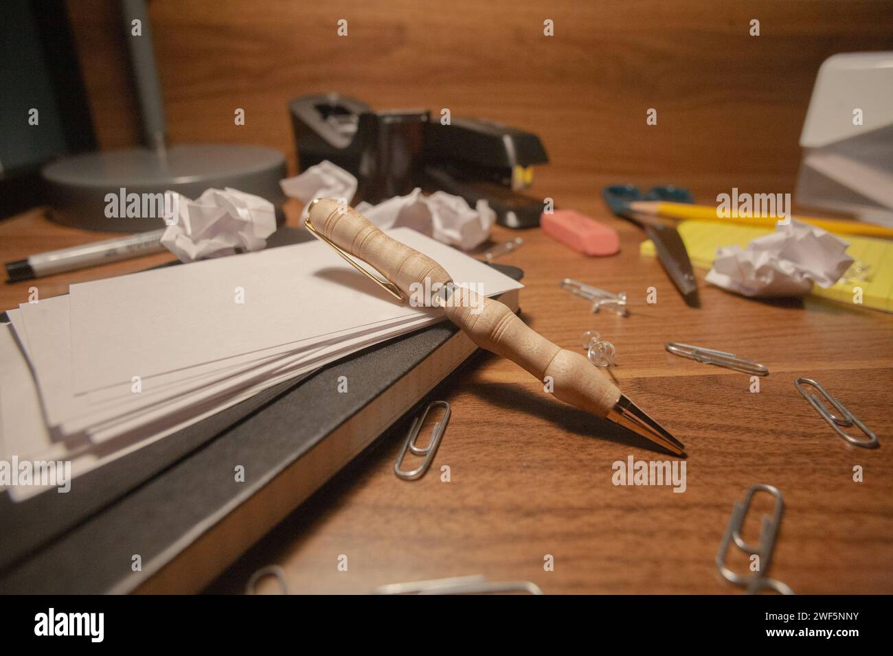 Una penna di legno su una scrivania disordinata con carta dappertutto Foto Stock