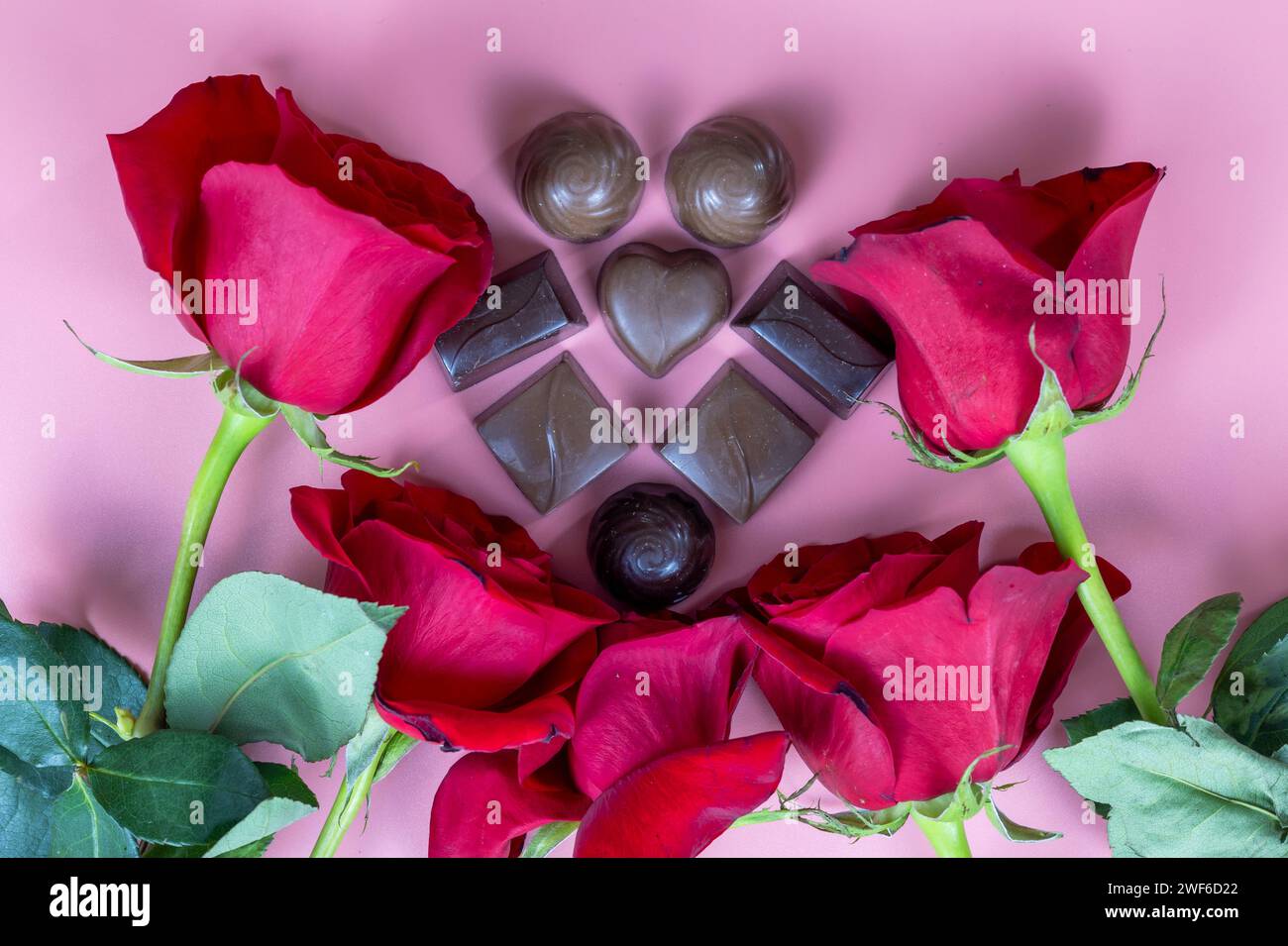 Deliziosi dolci al cioccolato e rose rosse su sfondo rosa Foto Stock