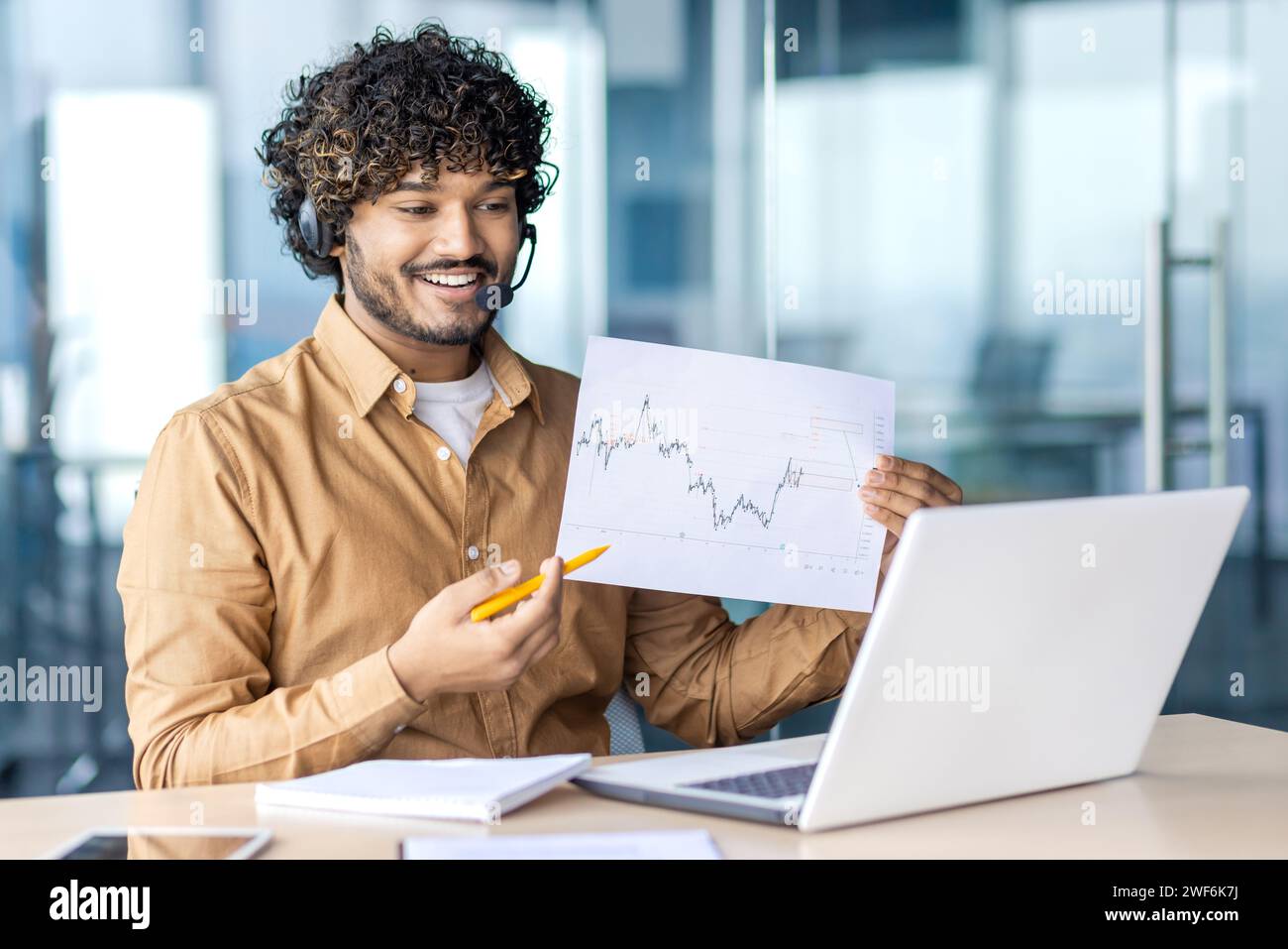 Ottimista datore di lavoro ispanico in videoconferenza con cuffie wireless che mostra un grafico statistico con risultati impressionanti. Responsabile del reparto marketing che condivide i risultati di una strategia di successo. Foto Stock