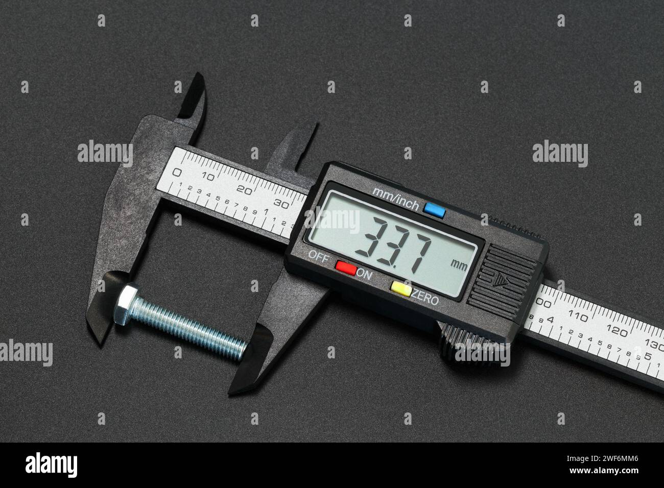 Misurazione della lunghezza del bullone con un calibro digitale. Fotografia macro su sfondo scuro Foto Stock