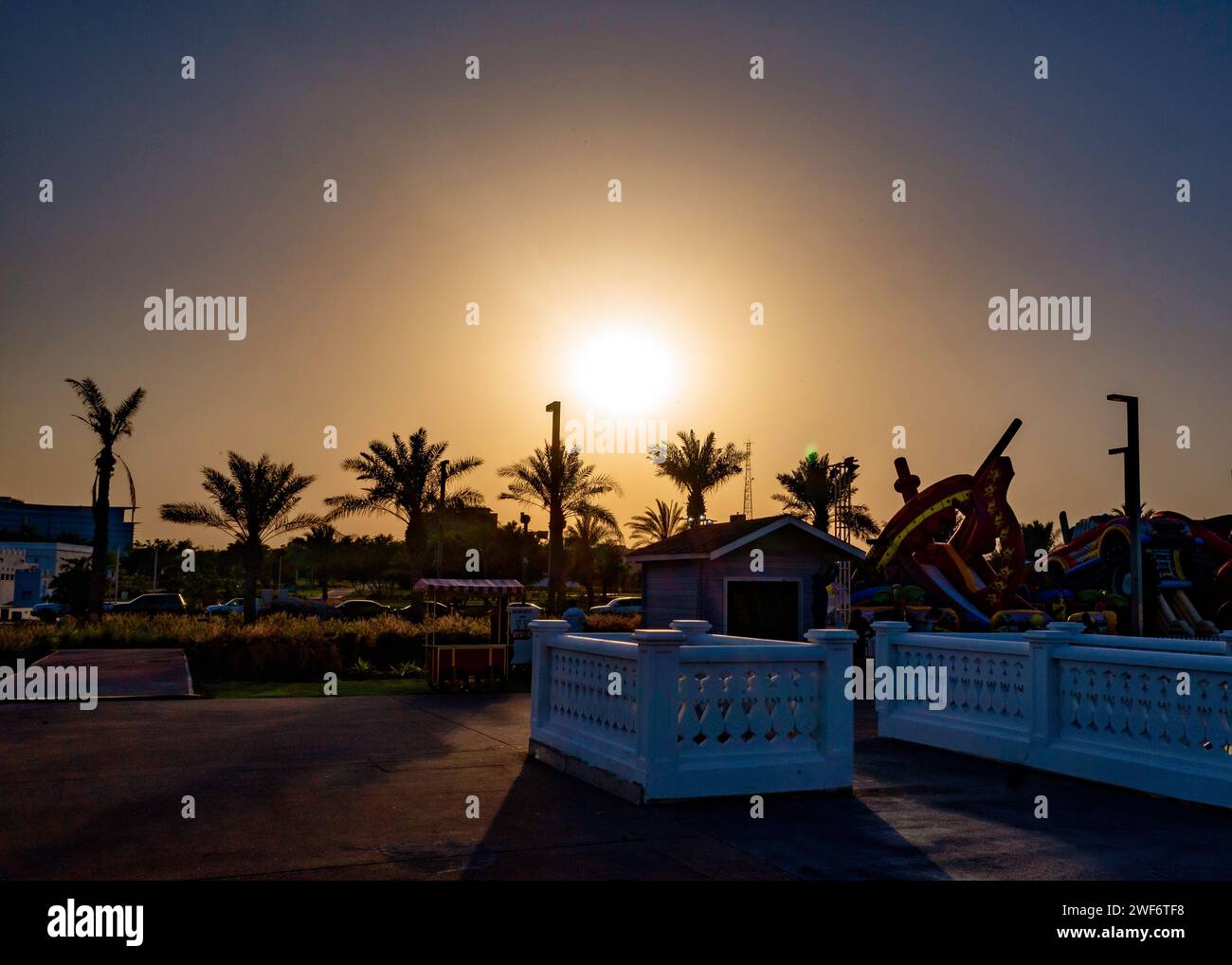 Panchina e sedia posizionate vicino alle palme di fronte ad un edificio: Vista del tramonto dal Parco al Bidda, Doha, Qatar Foto Stock