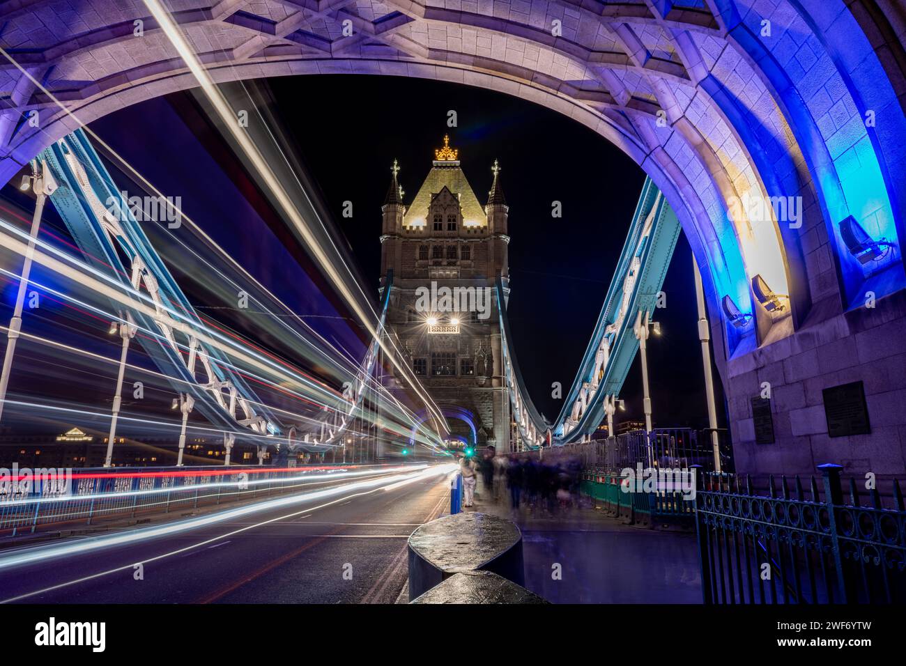 Una lunga esposizione notturna scattata sul Tower Bridge con un pedone, i turisti che visitano questo iconico monumento e i sentieri luminosi dai veicoli di passaggio. Foto Stock