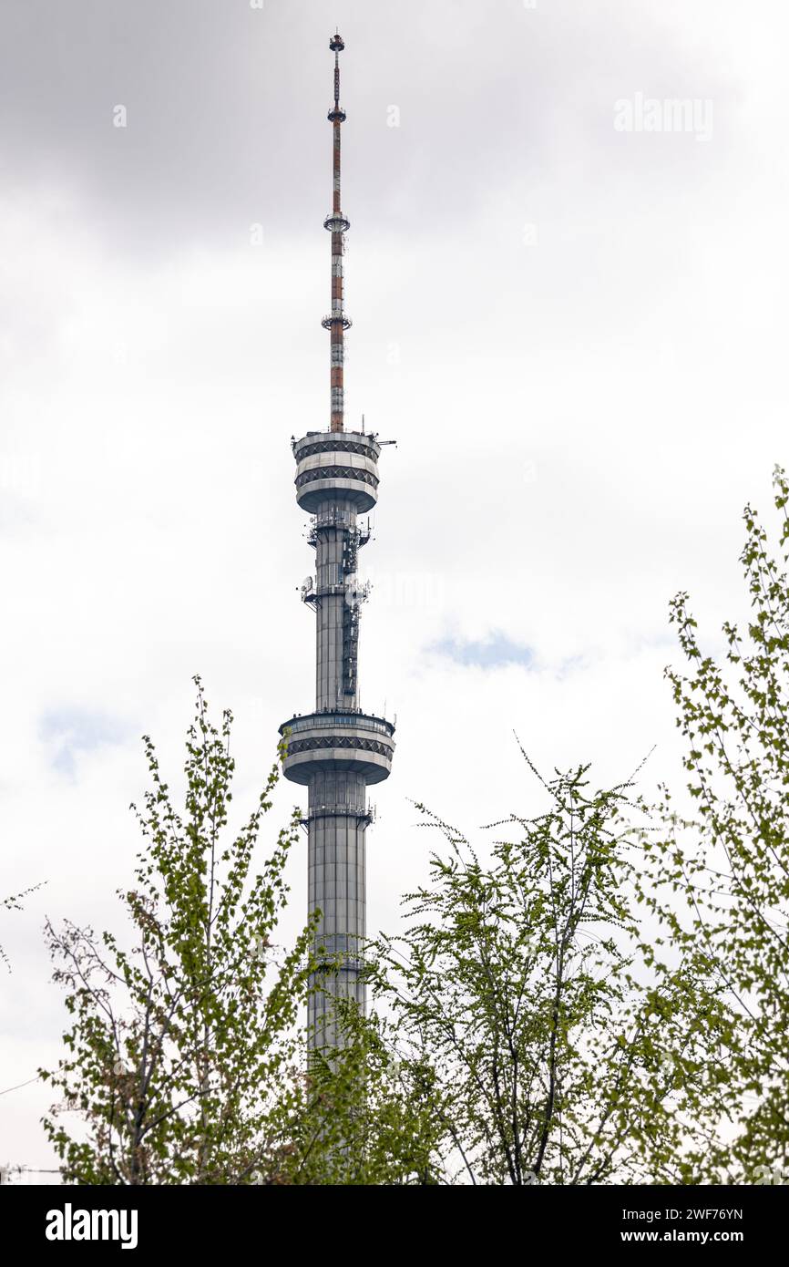 Alto e grande edificio con vista della torre della televisione attraverso i rami degli alberi. struttura dell'antenna sotto forma di torre sulla quale vengono trasmesse le antenne per la televisione Foto Stock