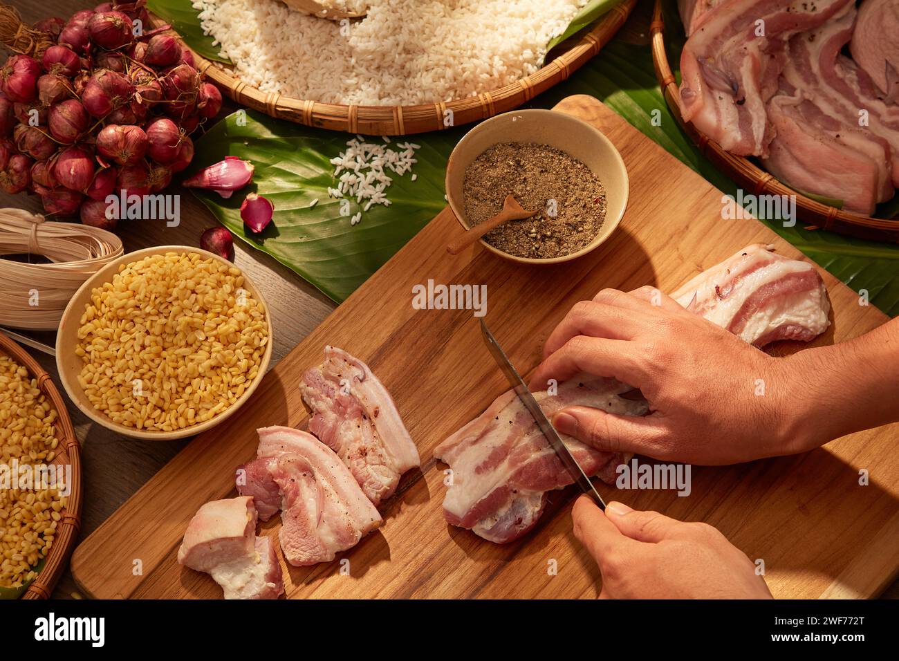 Il modello a mano sta tagliando il maiale come ingredienti per preparare la torta di riso appiccicosa (chung cake). Cibo tradizionale durante le vacanze Tet. Celebrazione del Capodanno cinese Foto Stock