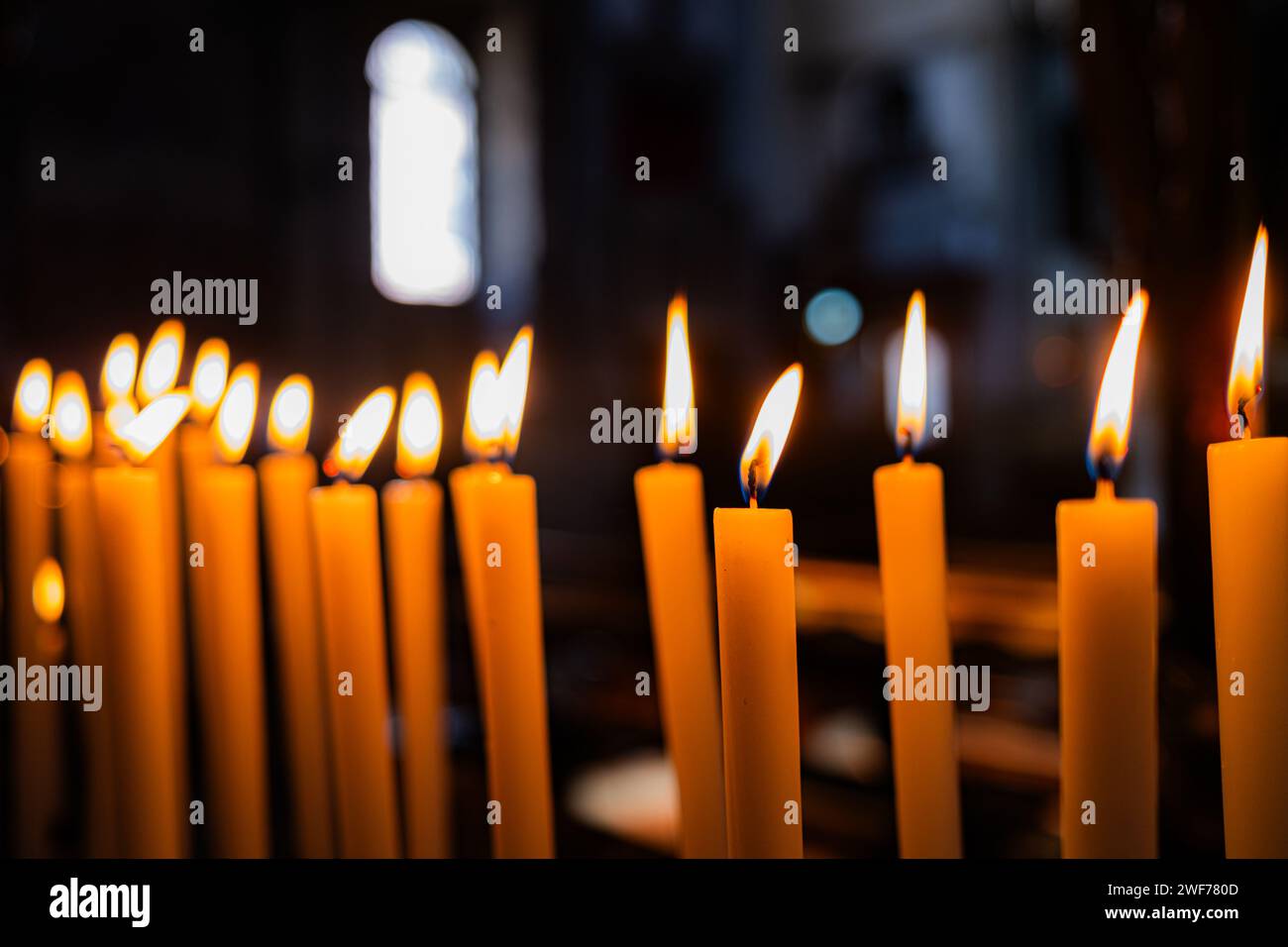 Primo piano di una fila di candele che offrono luce e calore nell'ambiente tranquillo di una chiesa. Foto Stock