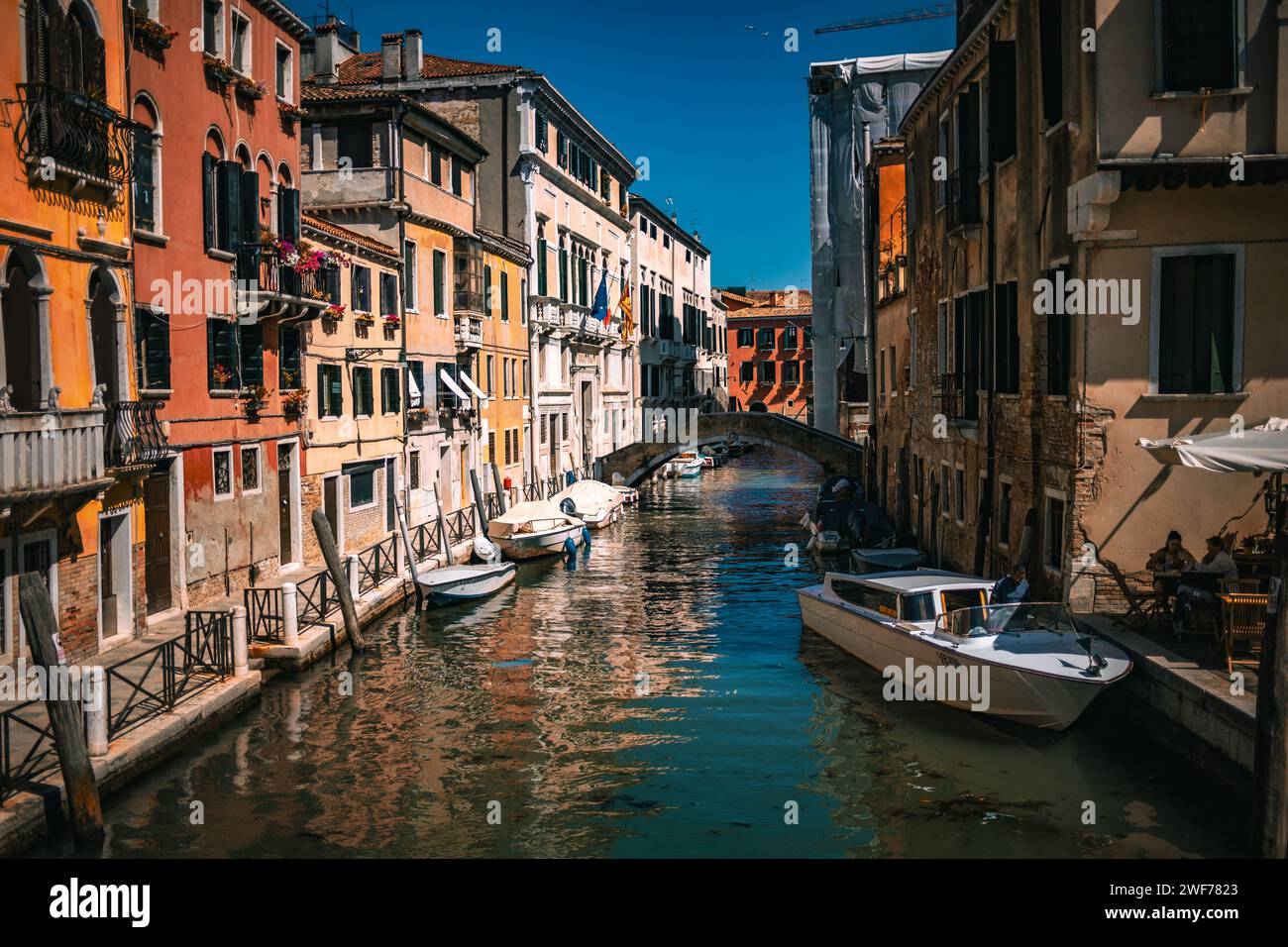 Un tranquillo canale veneziano fiancheggiato da colorati edifici storici e barche da diporto sotto il cielo azzurro di Venezia, Italia. Foto Stock