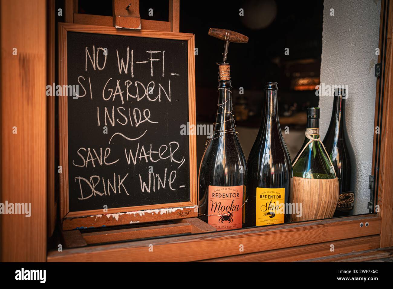 Una divertente lavagna fuori da un ristorante di Venezia invita gli ospiti a gustare un vino in WiFi, mettendo in risalto un giardino locale. Foto Stock