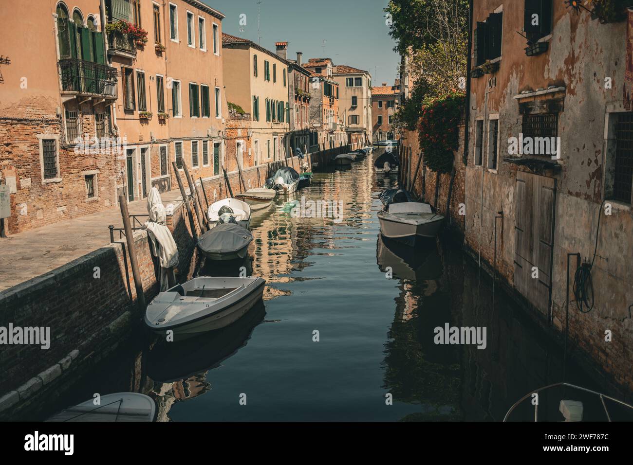 Le barche ormeggiate fiancheggiano un tranquillo canale residenziale circondato da tradizionali case veneziane in una giornata di sole. Foto Stock
