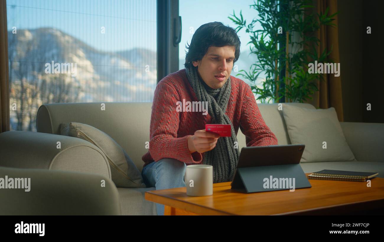 giovane con sciarpa che inserisce il numero di carta di credito sul tablet per acquistare beni a distanza, sicuro e facile pagamento elettronico a distanza mentre si trova Foto Stock