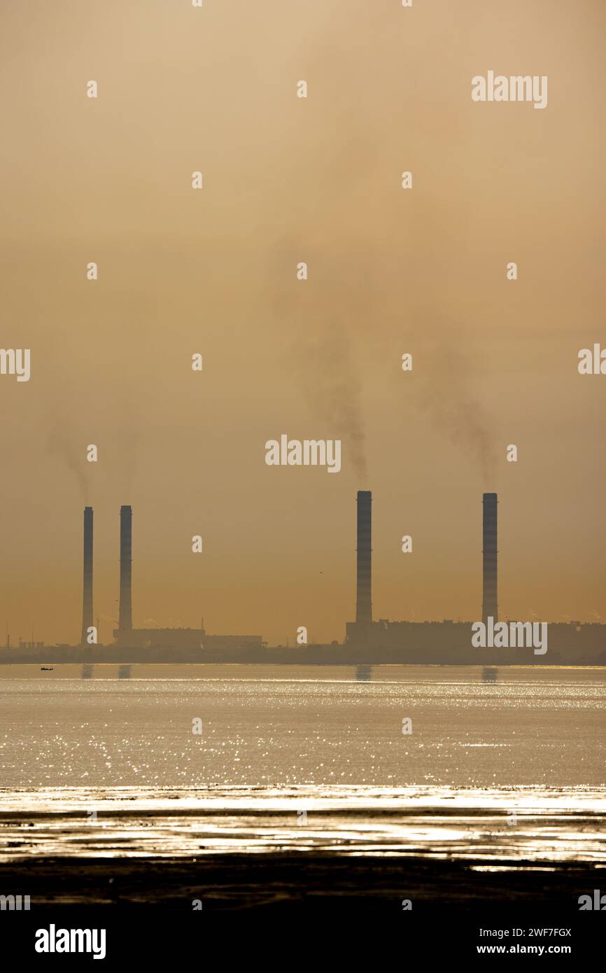 I fumogeni su un complesso industriale urbano, con un fiume sullo sfondo Foto Stock