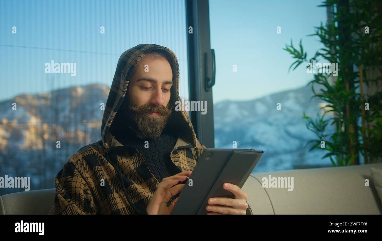 Ragazzo barbuto rilassarsi a casa sedersi sul tablet divano godere di navigare sul Web, studiare online, fare shopping su Internet, utilizzare le app dei social media. Moder Foto Stock
